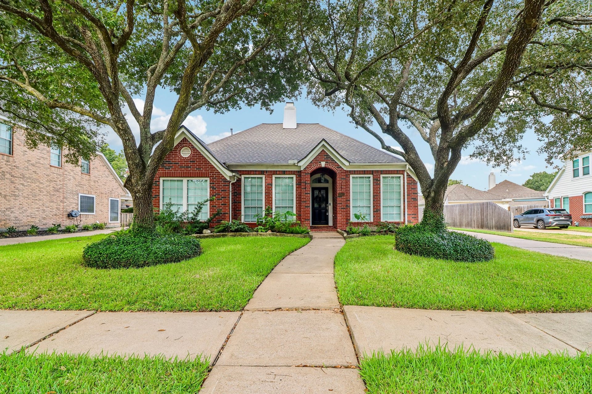 Charming red-brick exterior framed by mature shade trees, manicured landscaping, and a welcoming covered entry.