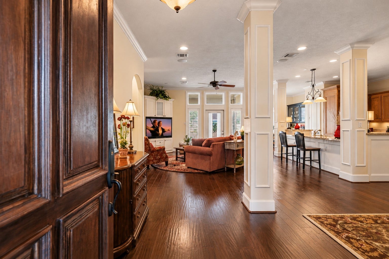 4631 Lake Village Drive, Fulshear, TX 77441 A sense of grandeur unfolds upon entry, where soaring ceilings, rich crown molding, continuous wood flooring, and stately cased columns set the tone for the home's refined design. Sunlight pours through expansive windows and dramatic transoms, illuminating the open living spaces with a warm, inviting glow.