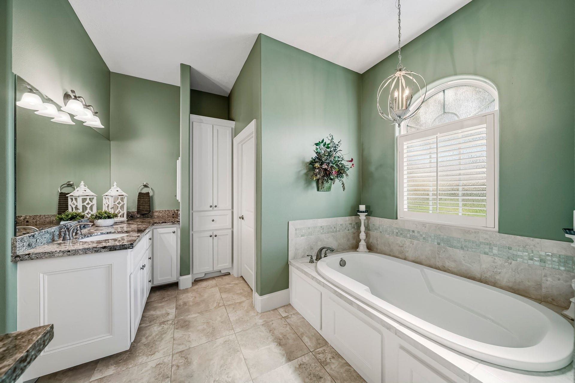 4631 Lake Village Drive, Fulshear, TX 77441 Indulge in a restorative escape within the oversized soaking tub, where soft mood lighting sets the stage for relaxation and rejuvenation. Overhead, an elegant arched transom crowns the window, adding architectural charm and inviting natural light into the space. Plantation shutters offer effortless privacy control, creating a serene sanctuary designed for quiet moments of luxury.