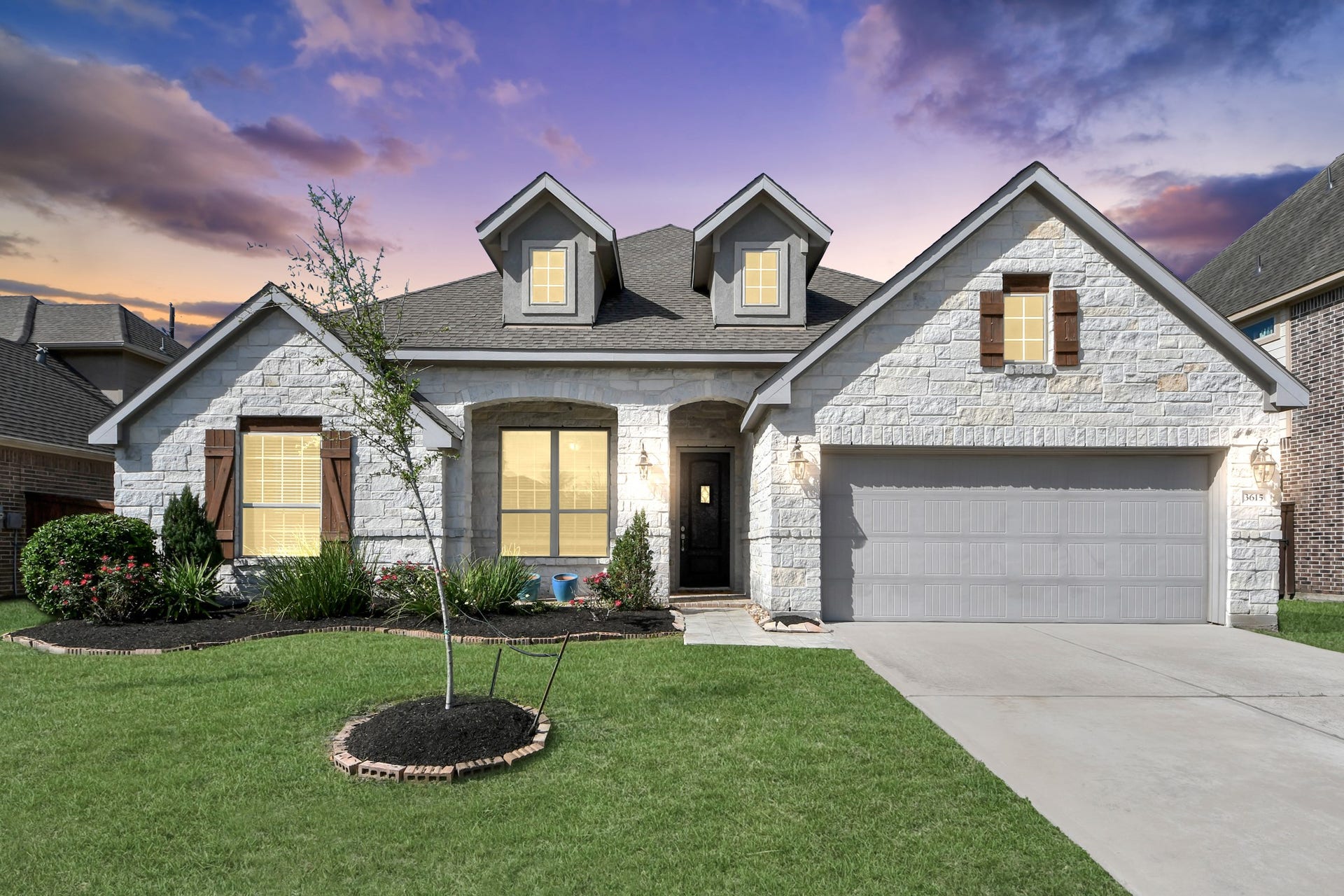 This charming home features a modern stone facade with a two-car garage and attractive landscaping. The inviting entrance and well-maintained lawn enhance its curb appeal, ideal for a welcoming family home.