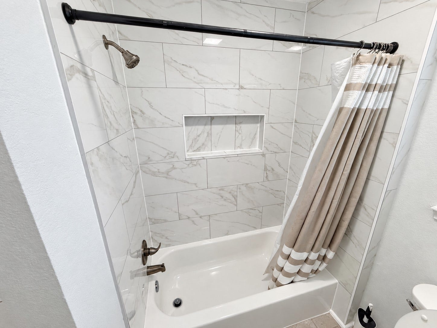 Tub/shower combination featuring marble-look tile and a recessed storage niche.