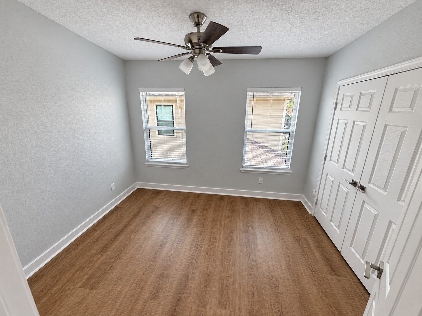 Bedroom with two windows, wood-look flooring, a ceiling fan, and a double-door closet.