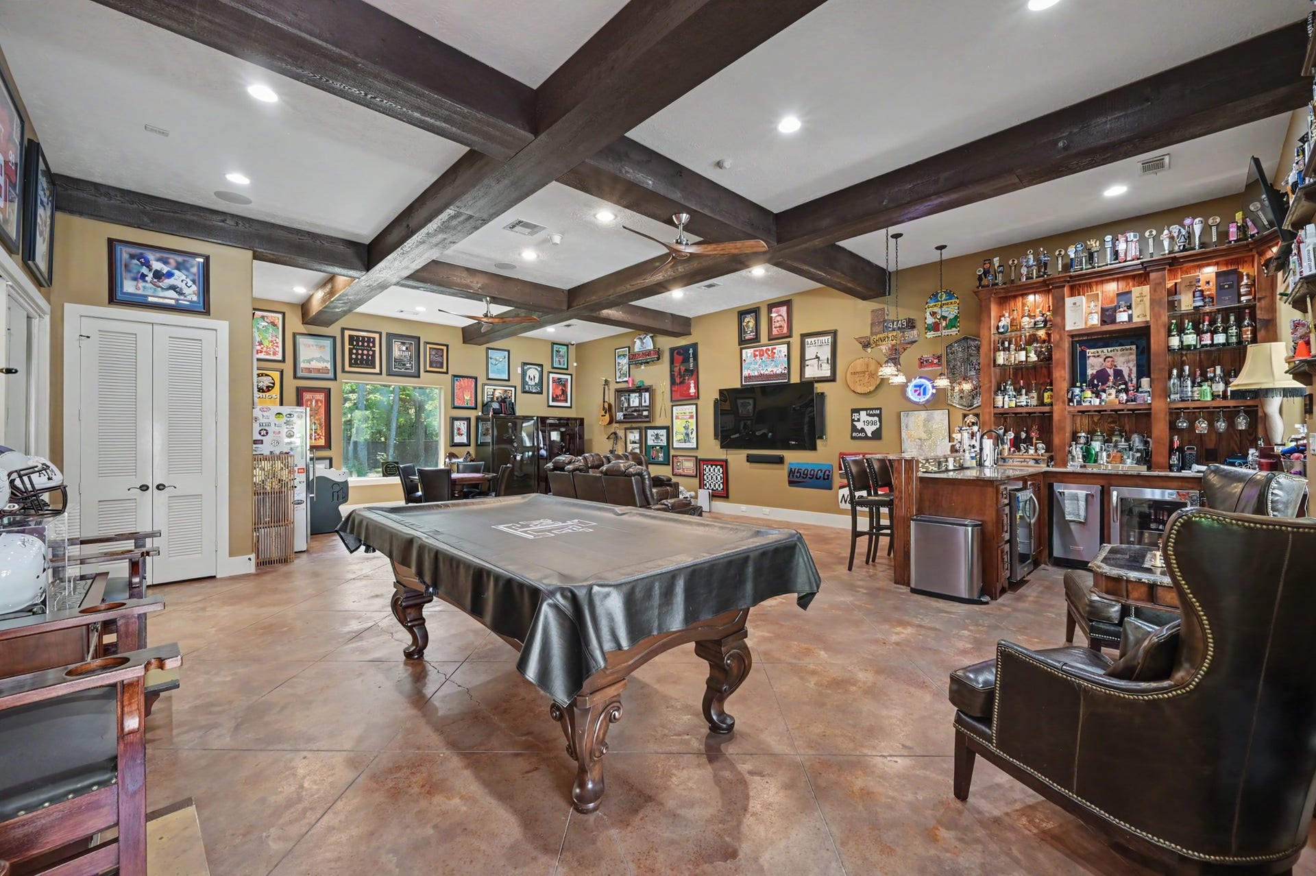 27706 Braydon Court, Spring, TX 77386 Spacious entertainment room featuring a billiards table, custom bar, and rich wood beam ceiling. Decorated with sports memorabilia, it offers a perfect setting for leisure and gatherings.