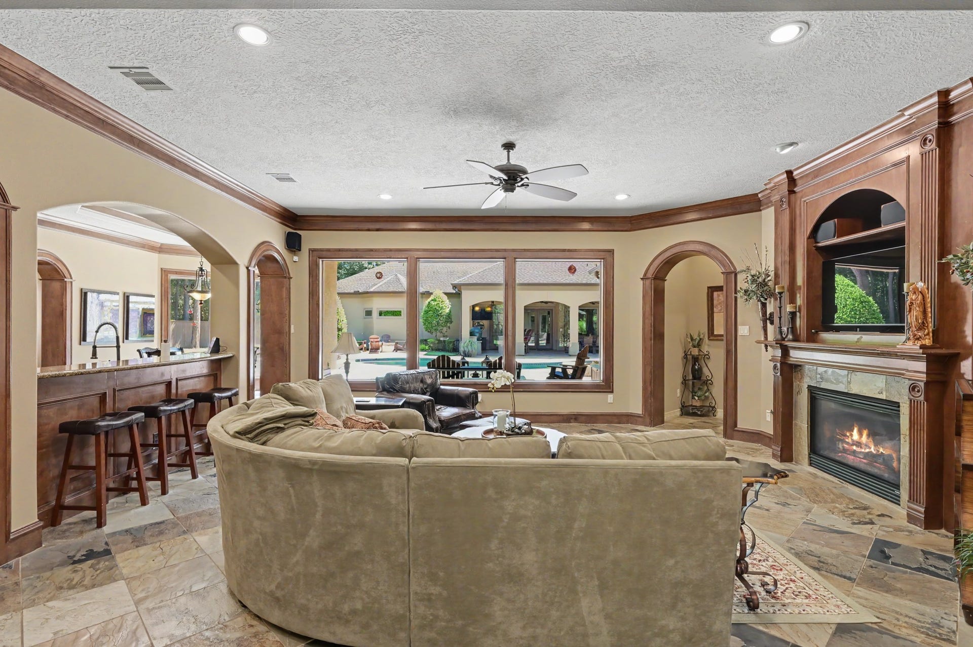 27706 Braydon Court, Spring, TX 77386 Spacious living area with a cozy fireplace, large windows offering pool views, and an open layout leading to a stylish kitchen bar with seating.
