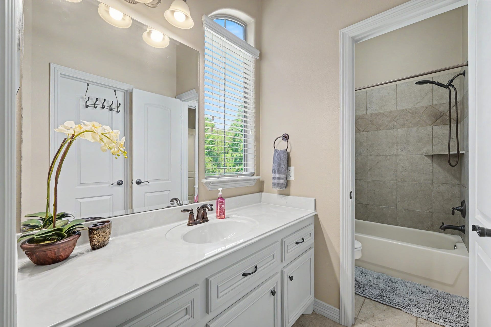 27706 Braydon Court, Spring, TX 77386 Bright and inviting bathroom featuring a spacious vanity with elegant fixtures, soft lighting, a large mirror, and a tiled shower-tub combo.