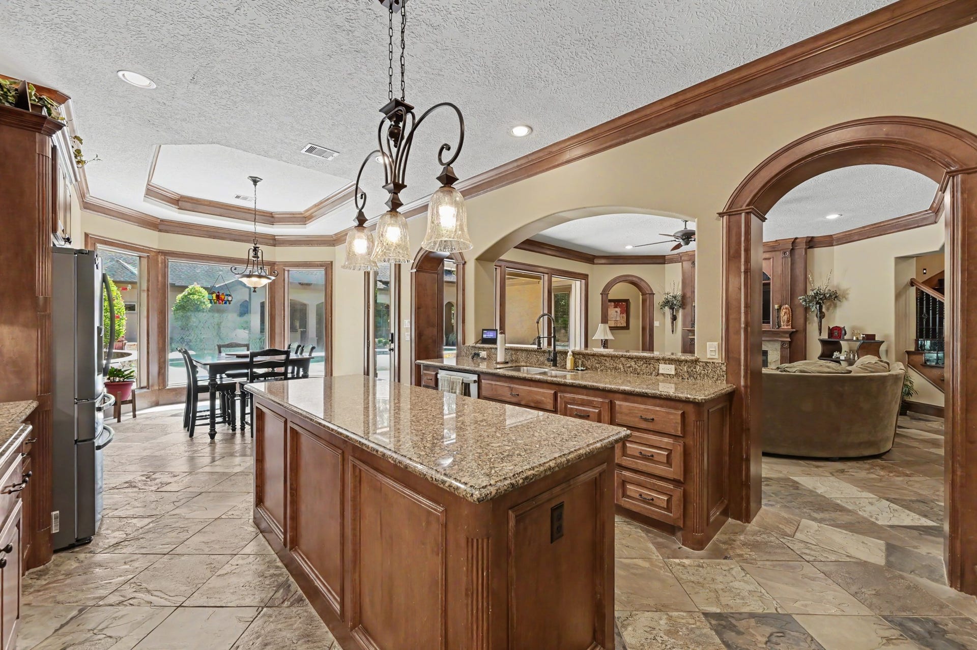 27706 Braydon Court, Spring, TX 77386 Spacious kitchen with elegant granite countertops, rich wood cabinetry, and a large island. The open layout flows seamlessly into a bright breakfast and family room area featuring abundant natural light from large windows overlooking the patio.