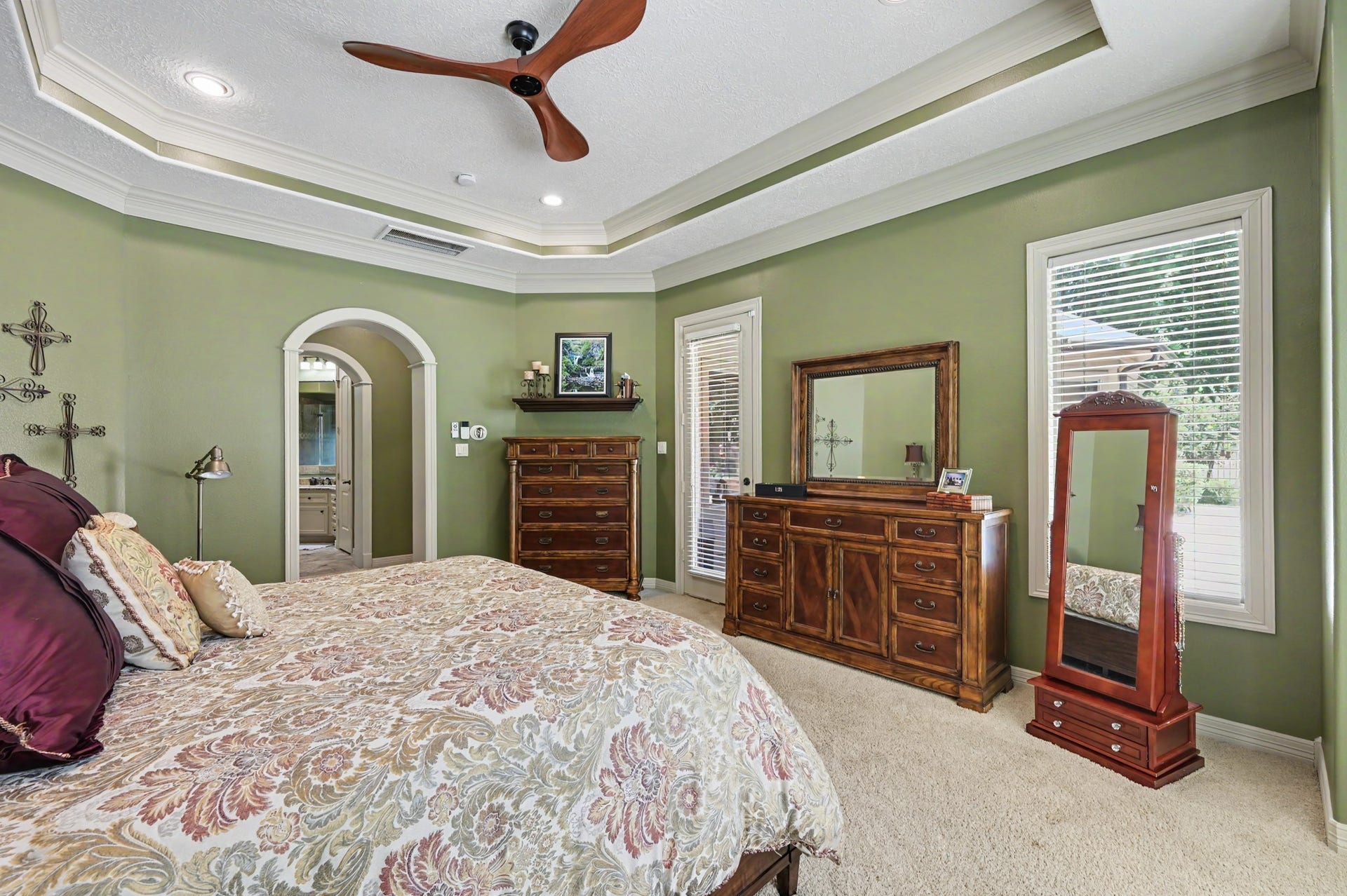 27706 Braydon Court, Spring, TX 77386 Primary, first floor bedroom featuring a tray ceiling with recessed lighting, large windows for natural light, a ceiling fan, and an ensuite bathroom through an arched doorway.