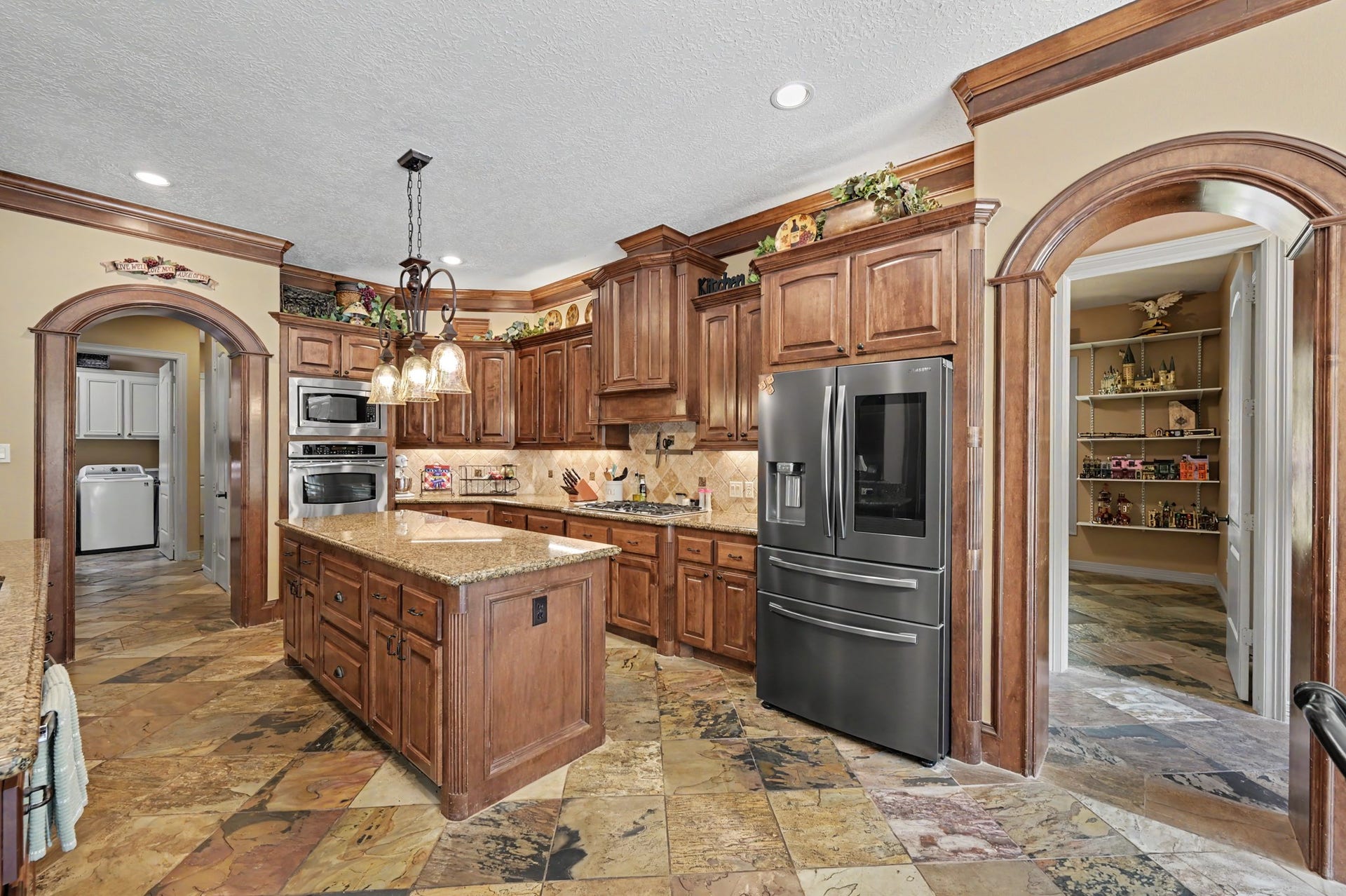27706 Braydon Court, Spring, TX 77386 Chef's style kitchen with rich wood cabinetry, granite countertops, and a central island. Stainless steel appliances enhance the space, while arched doorways add a touch of classic charm.