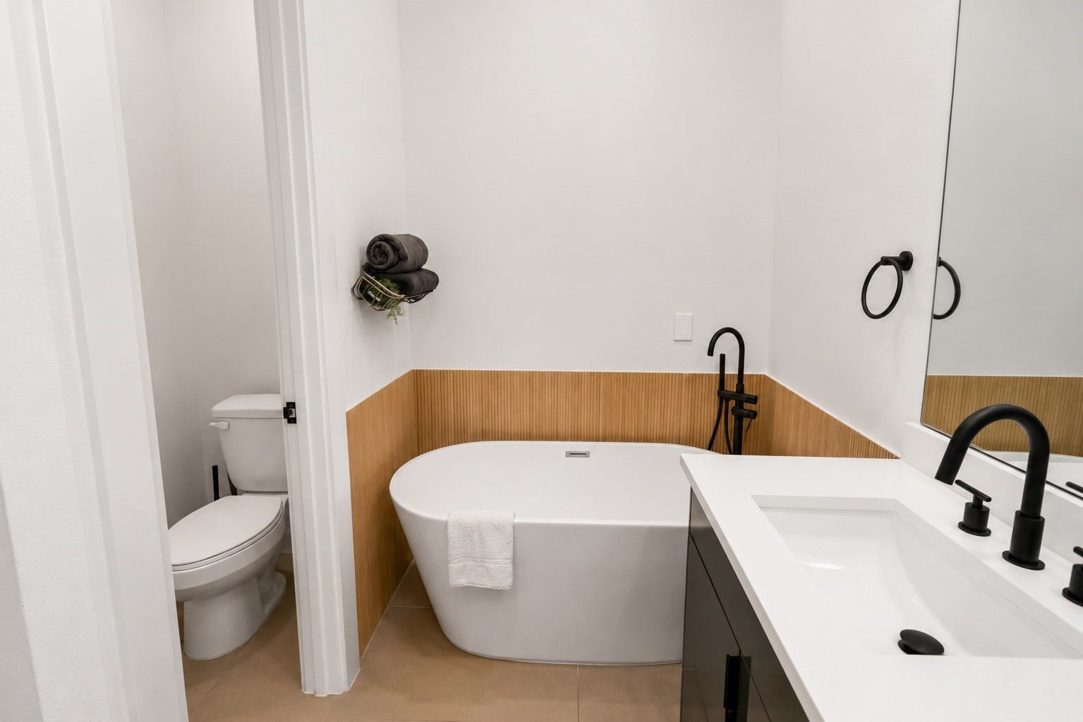 6742 Peerless Street, #B, Houston, TX 77021 Relax and recharge in a spa inspired primary bath featuring a freestanding soaking tub framed by warm fluted wood accent paneling, quartz countertops, and sleek matte black fixtures. A separate water closet and clean, contemporary finishes create a private retreat with timeless designer appeal.