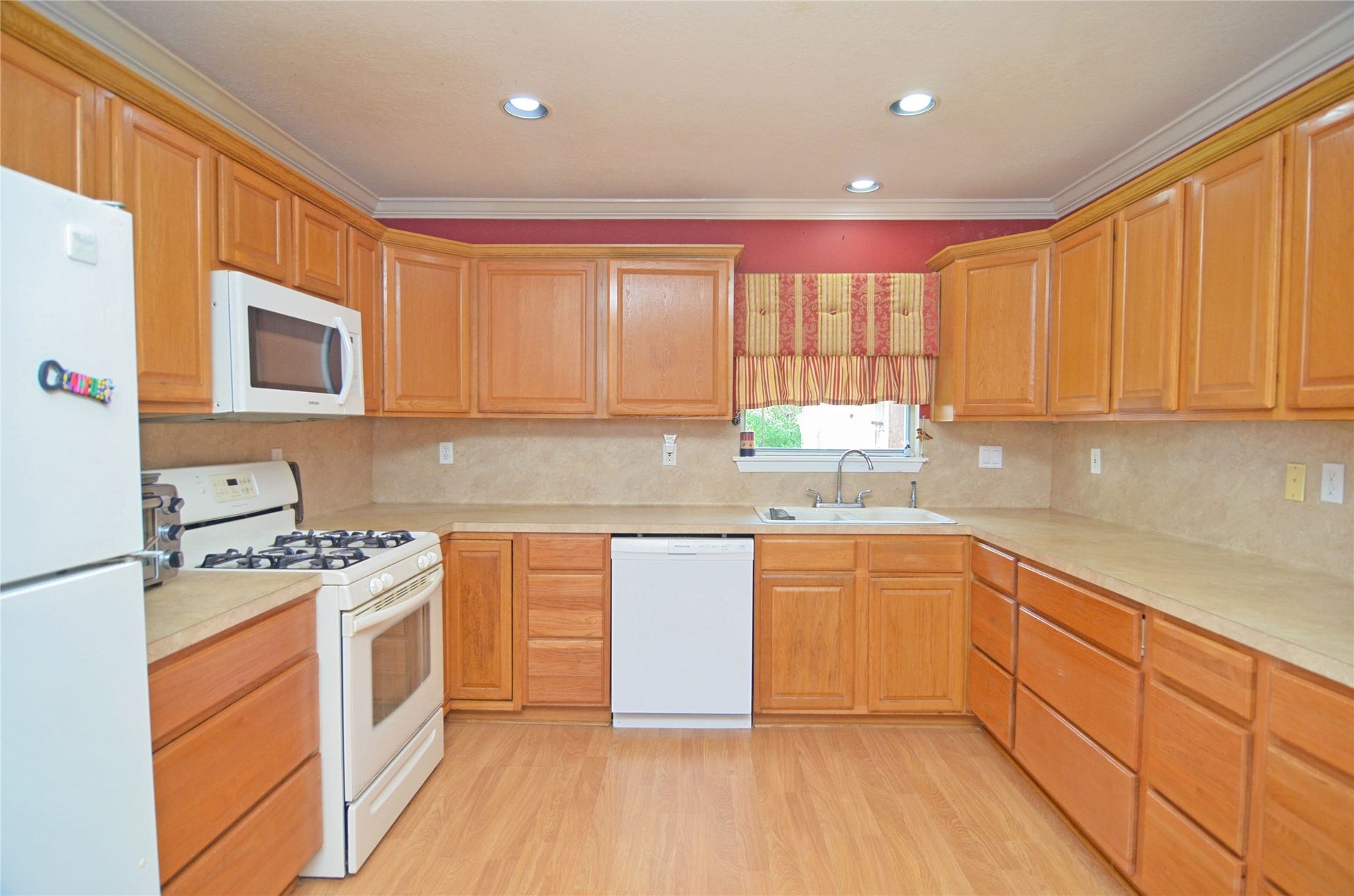 2719 Sweetgum Street, Pasadena, TX 77502 This kitchen features warm wooden cabinetry, a gas stove, and a built-in microwave. It includes a dishwasher, a double sink under a window, and recessed lighting, providing a bright and functional space.