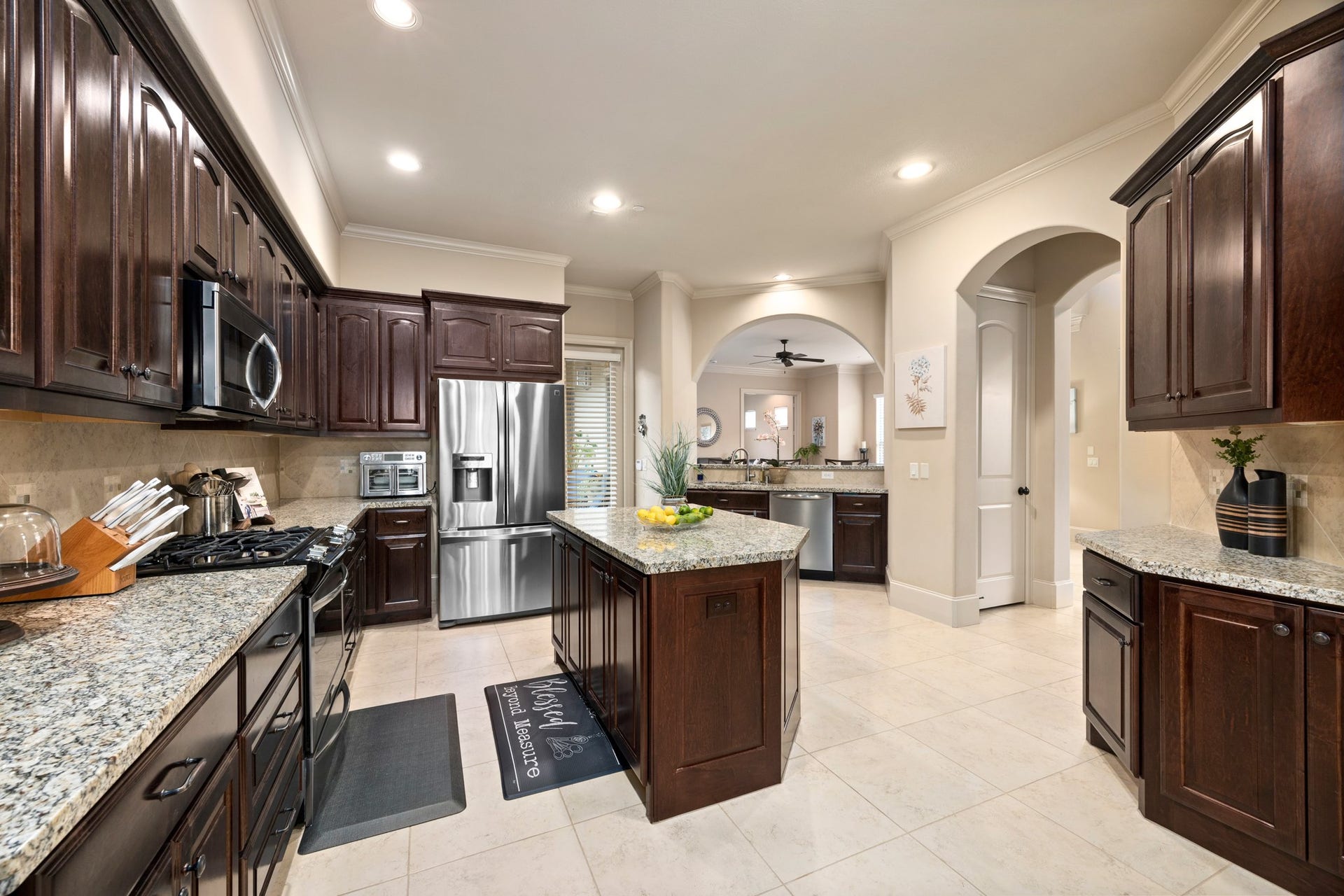 4315 Serenade Terrace Drive, Missouri City, TX 77459 This spacious kitchen features dark wood cabinetry, granite countertops, and stainless steel appliances. An island provides extra prep space, and the open layout connects to a living area through archways, enhancing the home's flow and natural light.