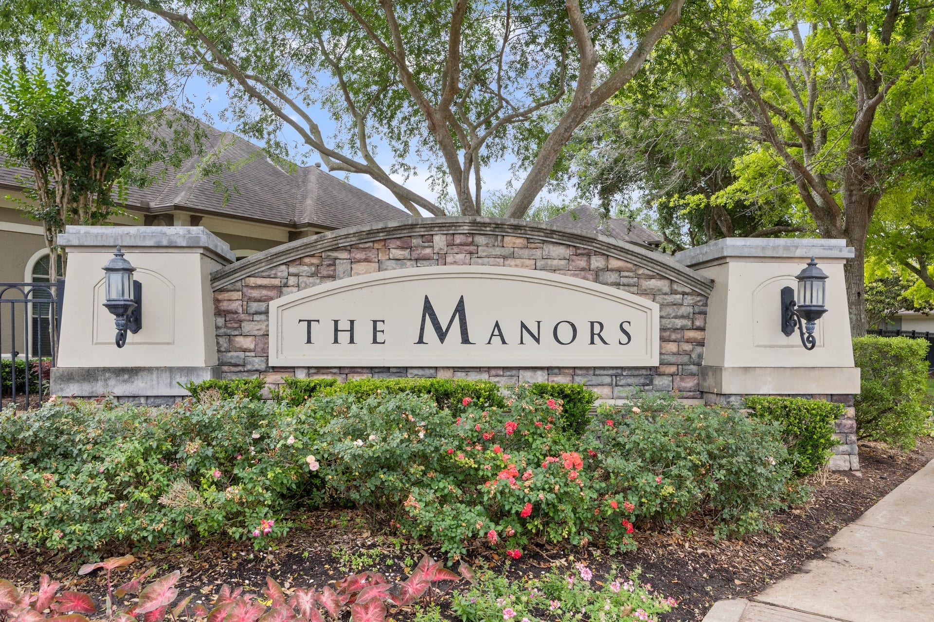 4315 Serenade Terrace Drive, Missouri City, TX 77459 This photo showcases the entrance to "The Manors," featuring a stylish stone sign with elegant lanterns. It's surrounded by well-maintained landscaping and mature trees, creating an inviting and upscale community atmosphere.