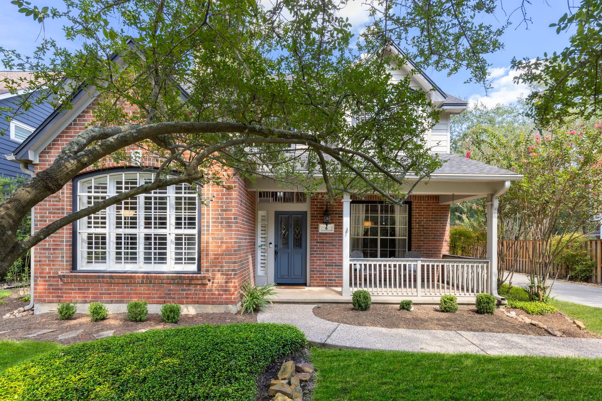 6 N Cochrans Green Circle, The Woodlands, TX 77381 Timeless brick faade framed by a sweeping mature oak, manicured beds, and a welcoming covered porch on a serene, tree-lined circle.