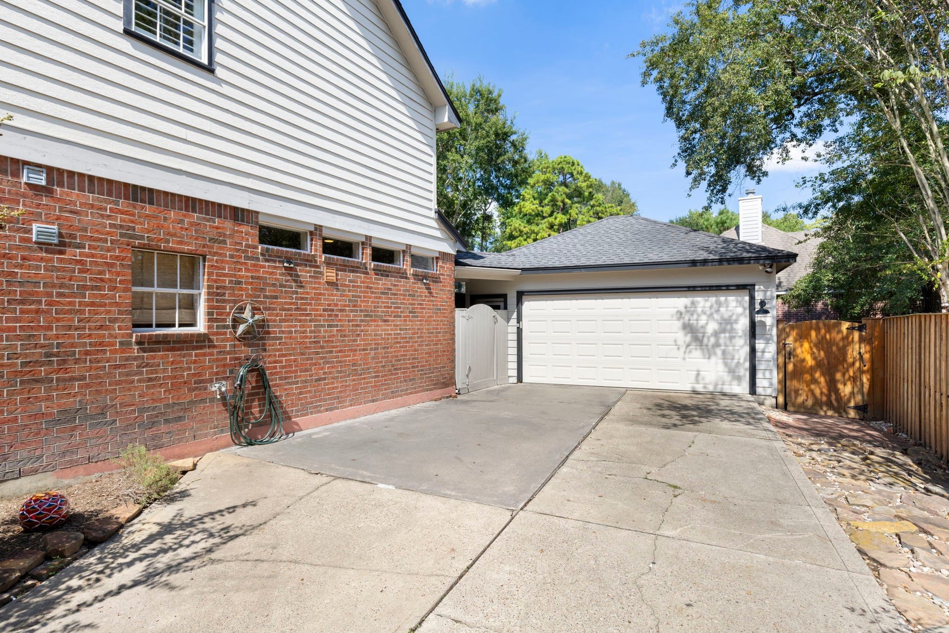 6 N Cochrans Green Circle, The Woodlands, TX 77381 Detached two-car garage with a generous extended driveway, bonus parking pad, and gated side access along a natural flagstone path.