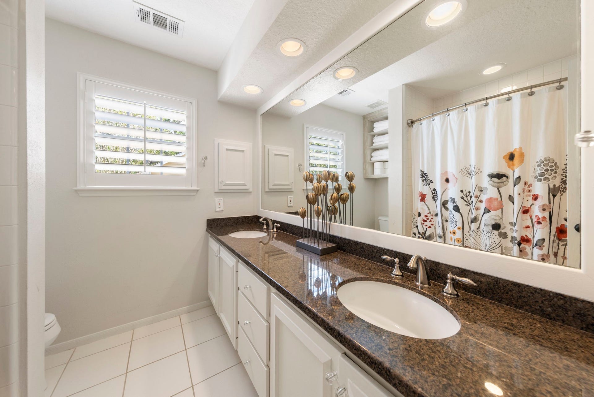 6 N Cochrans Green Circle, The Woodlands, TX 77381 Secondary bath offering a double-sink granite vanity, plantation shutters, built-in shelving, and a tub/shower combination.