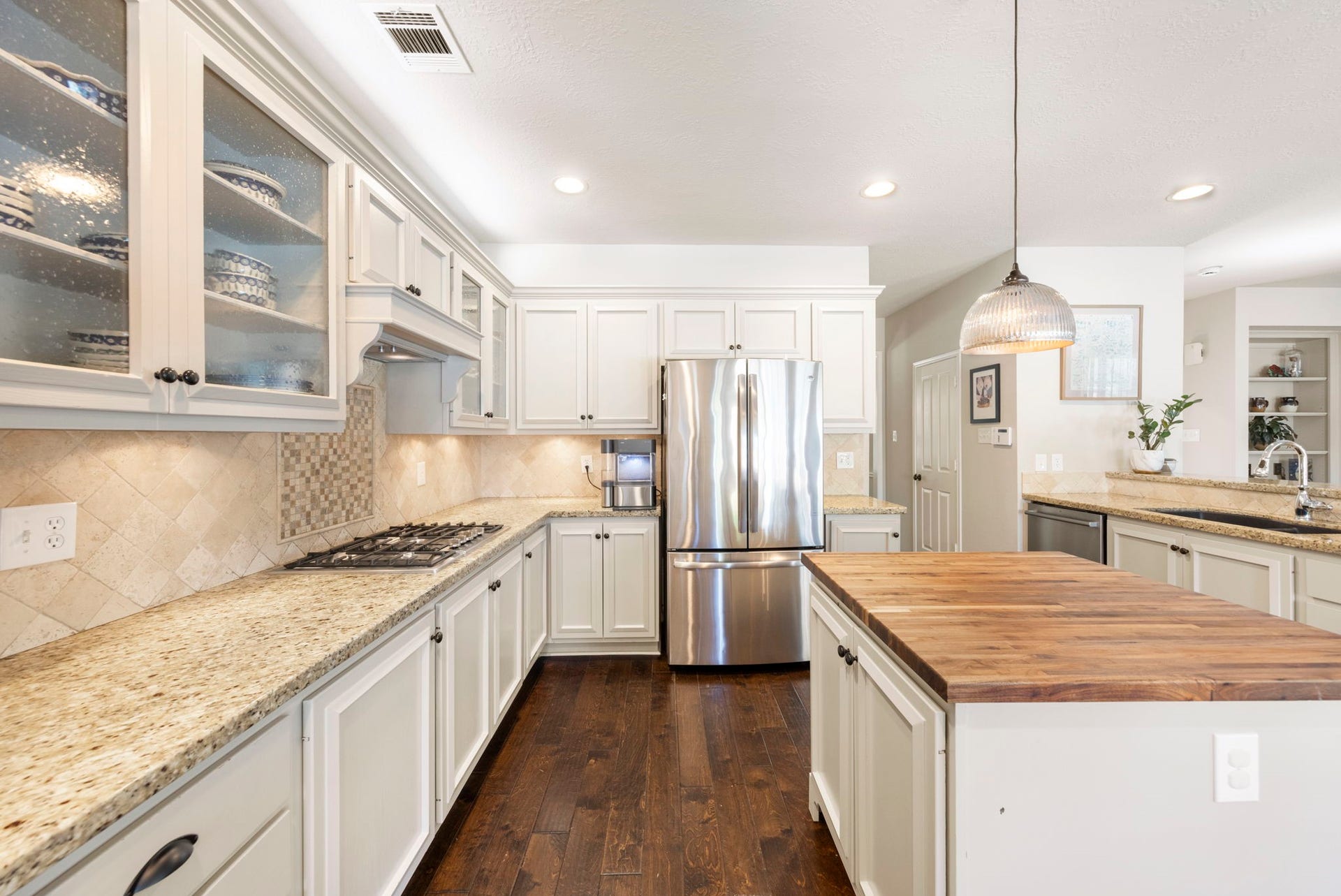 6 N Cochrans Green Circle, The Woodlands, TX 77381 Gas cooktop set against a travertine backsplash with mosaic inset, custom vent hood, under-cabinet lighting, and generous granite counters.