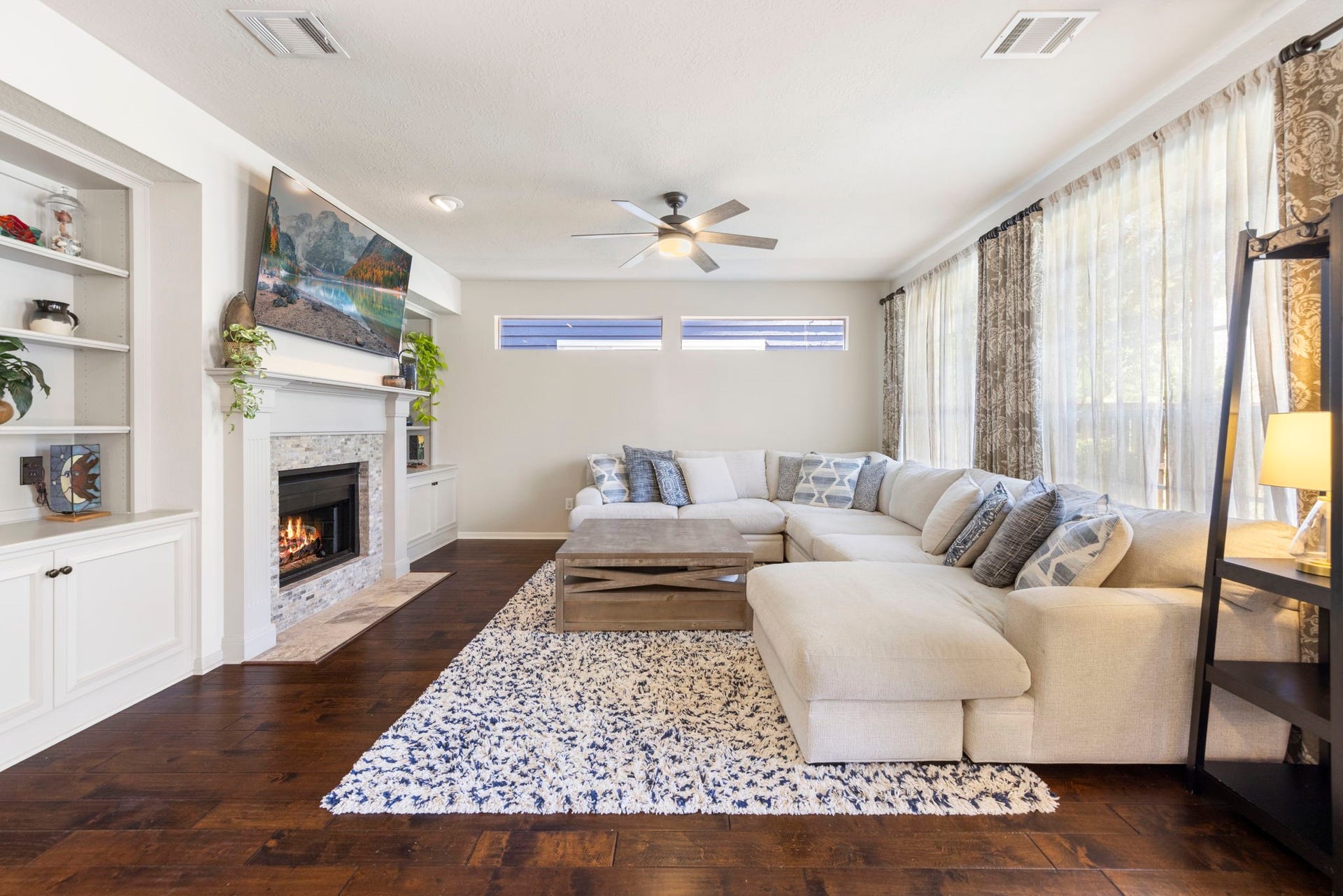 6 N Cochrans Green Circle, The Woodlands, TX 77381 Sun-drenched family room showcasing a stacked-stone fireplace flanked by custom built-ins, clerestory windows, and a wall of glass.