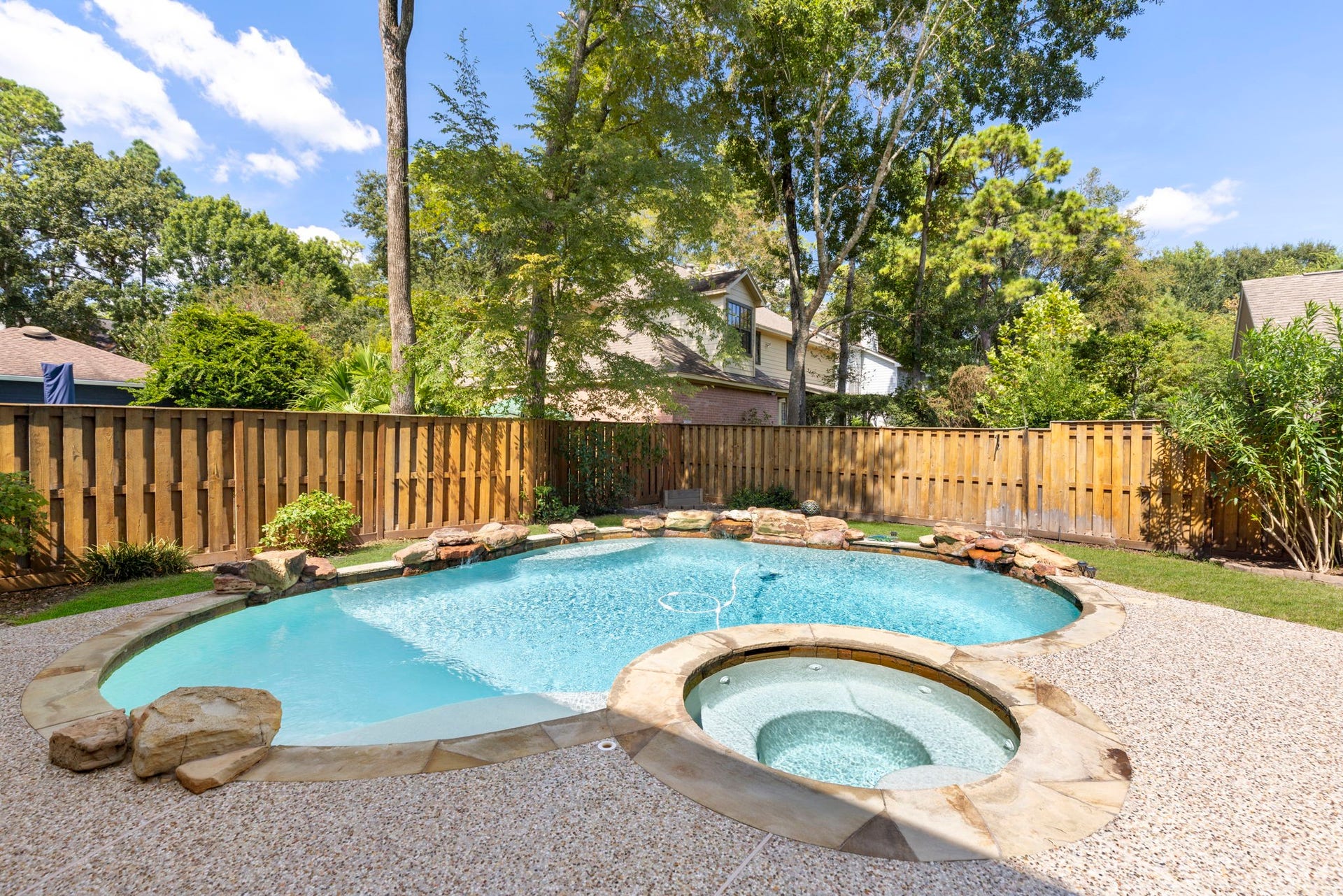 6 N Cochrans Green Circle, The Woodlands, TX 77381 Shimmering pool and raised spa trimmed in natural flagstone, with cascading boulder water features and board-on-board privacy fencing beneath towering pines.