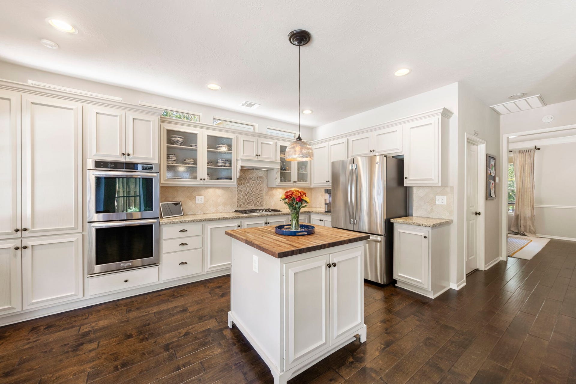 6 N Cochrans Green Circle, The Woodlands, TX 77381 Chef-inspired kitchen with bright white cabinetry, seeded-glass display fronts, stainless double ovens, and a warm butcher-block island.