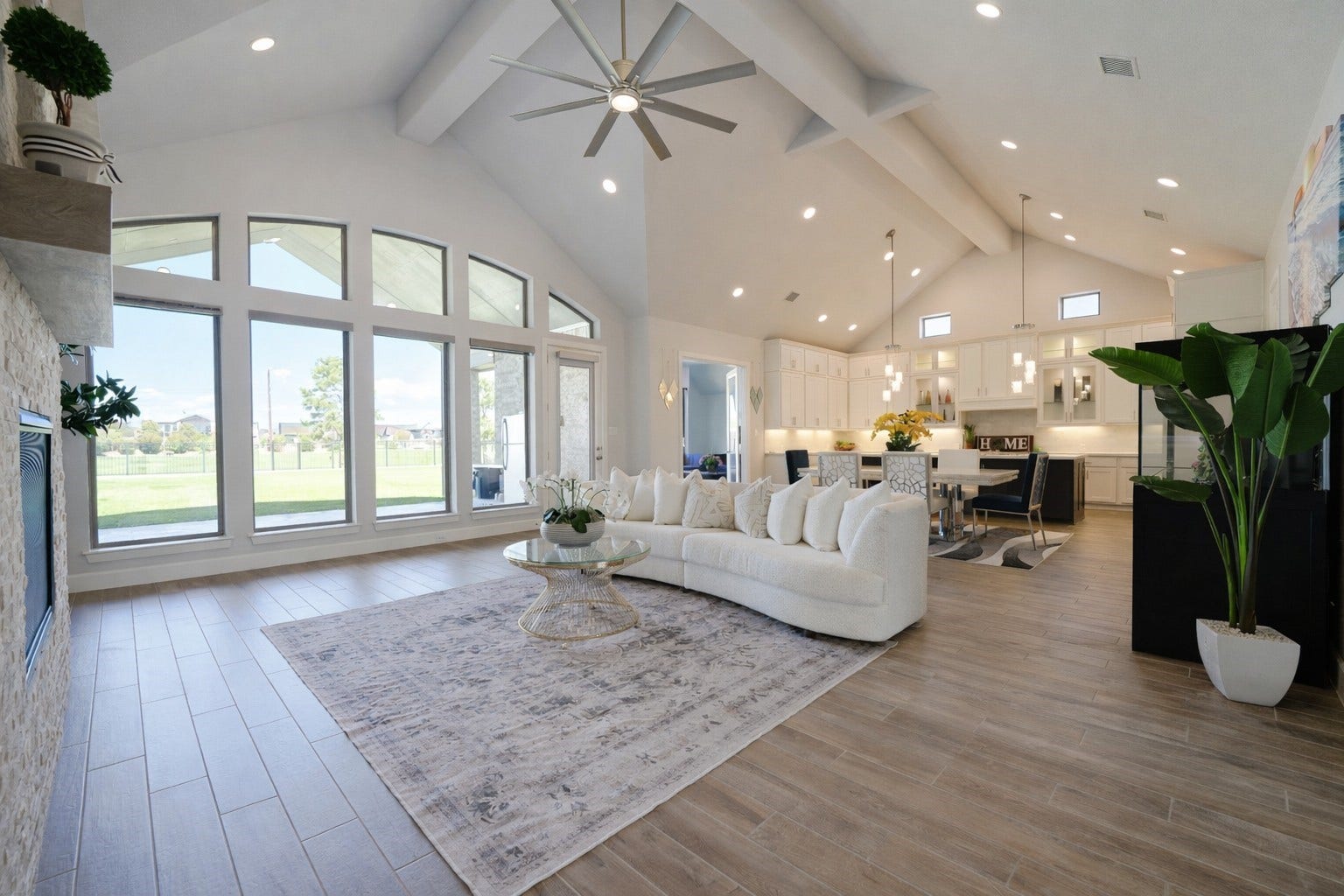 7707 Laurel Bloom Lane, Katy, TX 77493 This spacious open-concept living area features high vaulted ceilings, large windows offering abundant natural light, and a seamless flow into the modern kitchen. The room is tastefully decorated with a neutral color palette, a cozy fireplace, and elegant fixtures, creating a welcoming and sophisticated atmosphere.