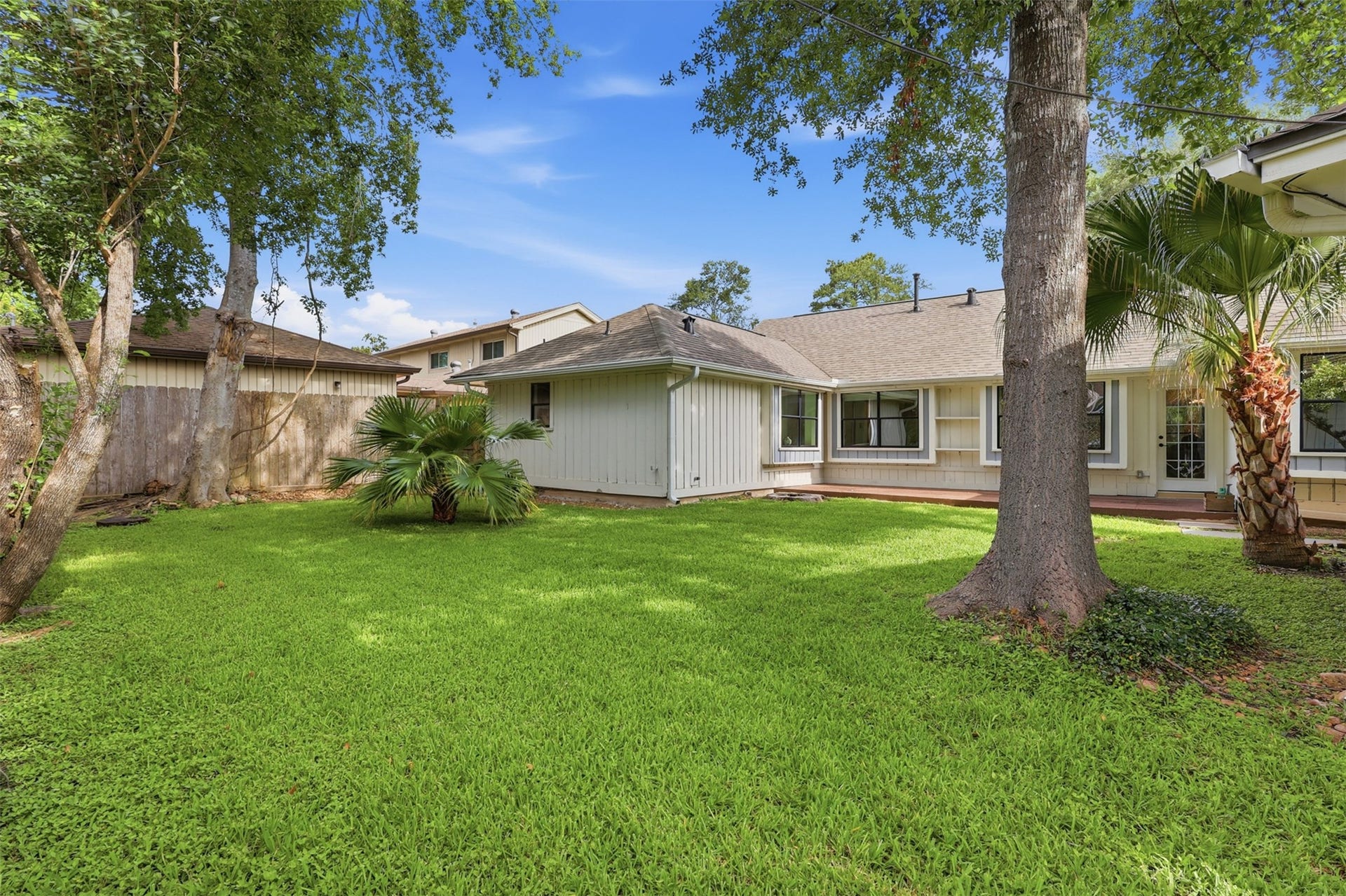 12523 Honeywood Trail, Houston, TX 77077 Fenced backyard with mature trees, green lawn, and a wood deck, offering outdoor space for relaxation and entertaining.