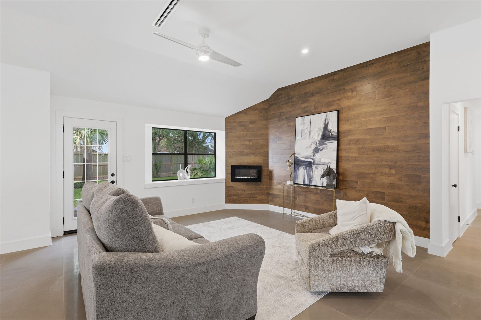 12523 Honeywood Trail, Houston, TX 77077 Spacious living room with a dramatic wood feature wall, modern fireplace, vaulted ceiling, and expansive window overlooking the backyard.