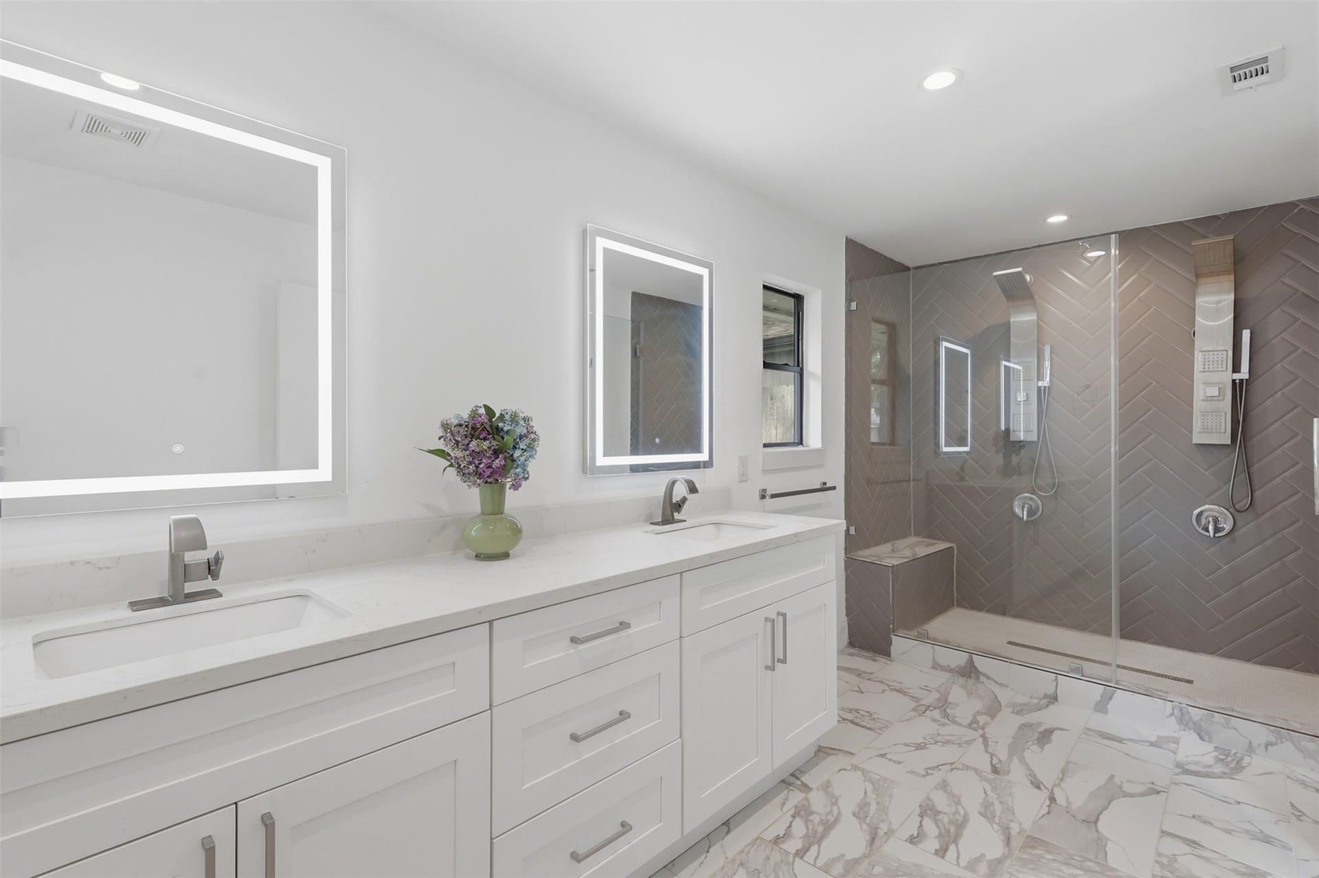 12523 Honeywood Trail, Houston, TX 77077 attached primary bathroom with double vanities, quartz countertops, walk-in shower with tile surround built-in bench, and glass enclosure. The space also includes recessed lighting, storge drawers, and a window for added natural light.