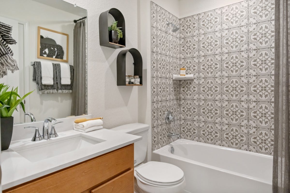 The secondary bathroom showcases tile flooring, a bath/shower combo with gorgeous Daltile tile surround, a stained vanity with stunning light countertop, large mirror, sleek fixtures, and contemporary finishes throughout.