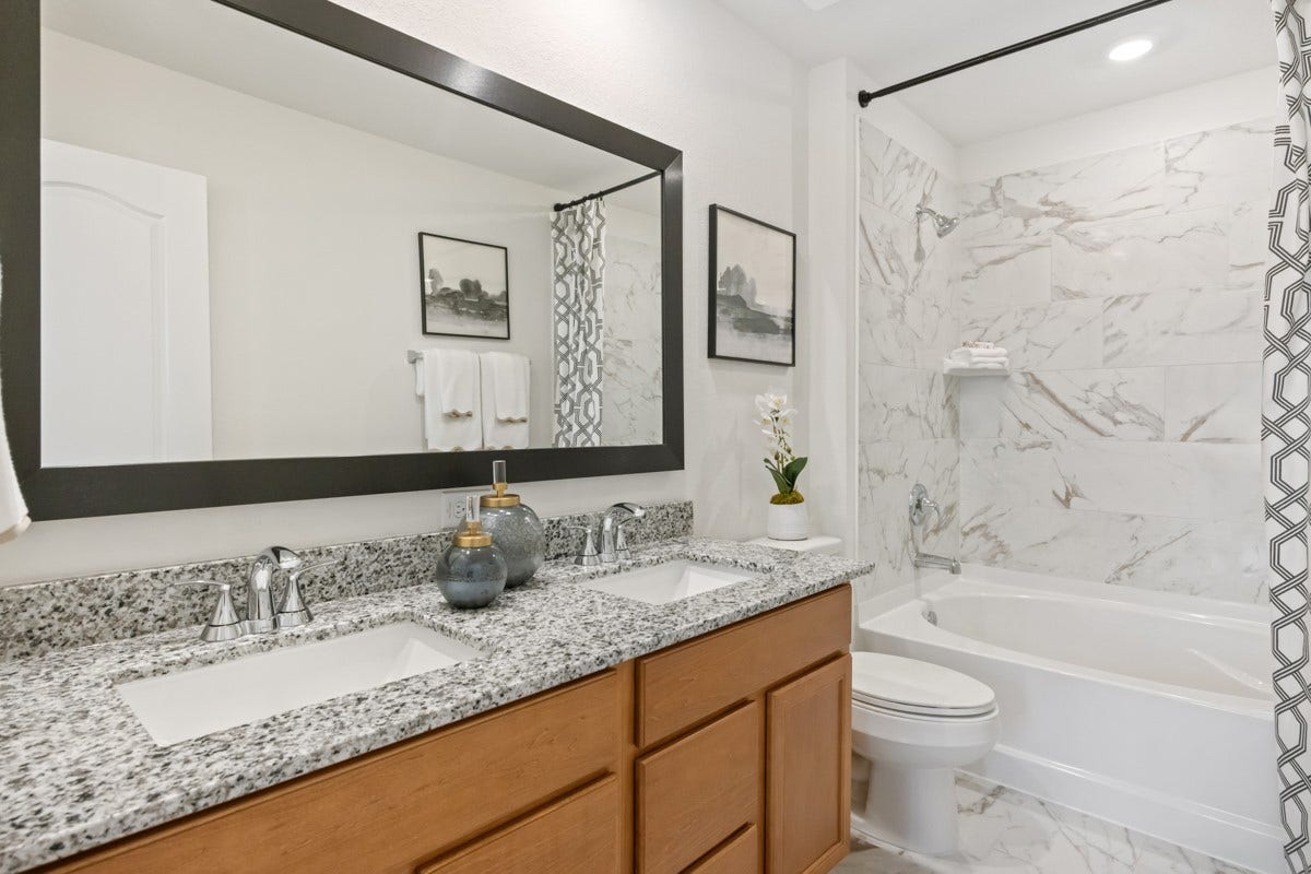 This beautifully updated primary bathroom is move-in ready! It showcases stained cabinetry paired with granite countertops, dual sinks, a large framed mirror, a spacious tub/shower combination with tile surround, high ceilings, custom paint, and stylish modern finishes throughout.