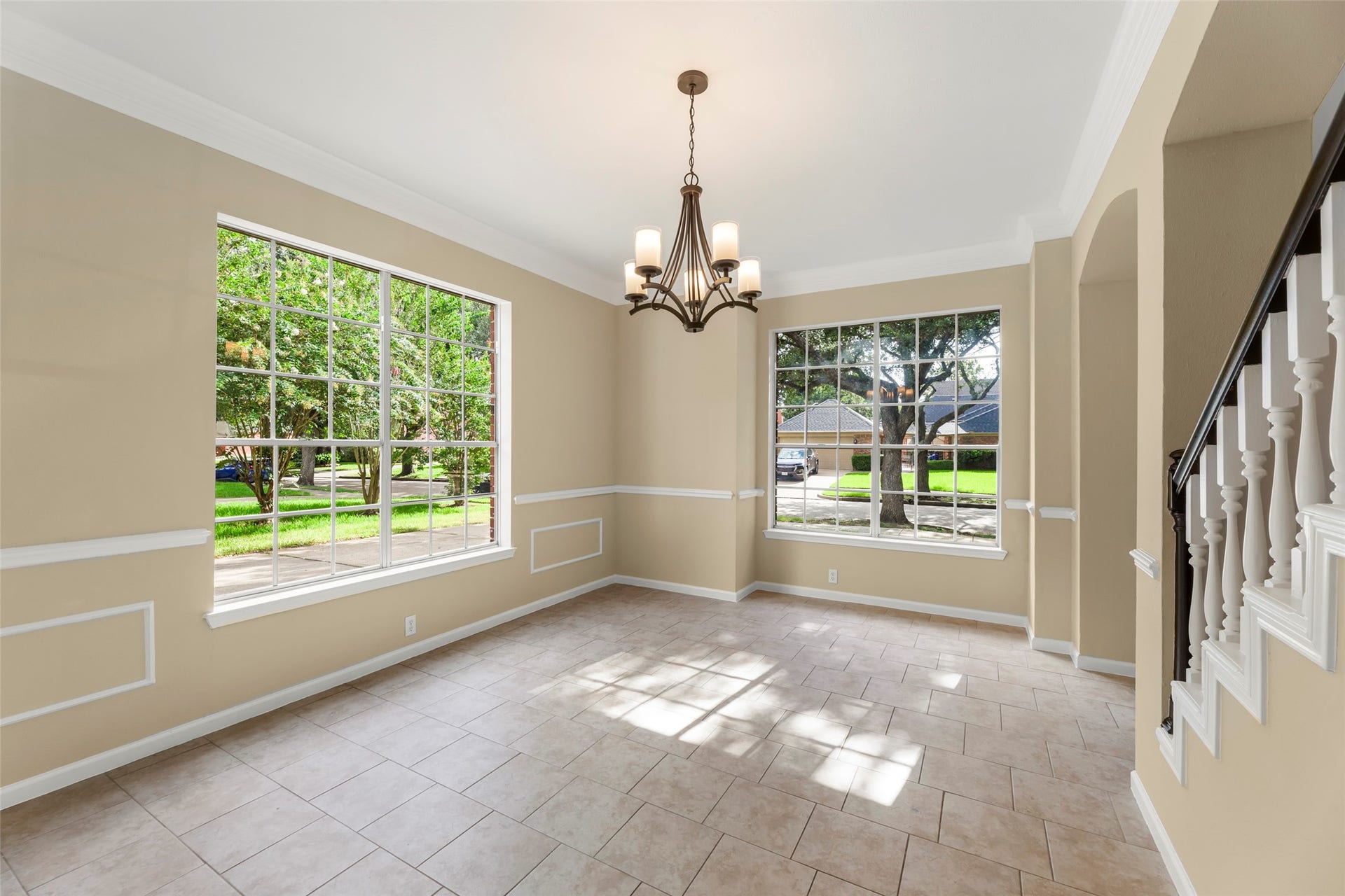 Natural light and views of the front yard. Features tiled floors, neutral walls, elegant trim, and a stylish chandelier. Perfect for a dining or living area.