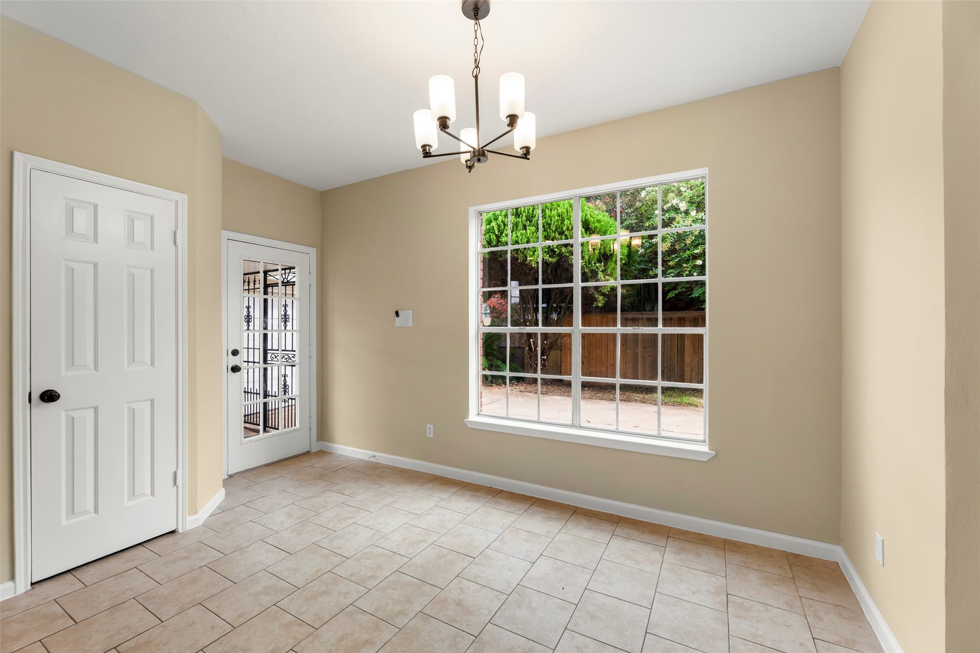 Overlooking a green backyard, tiled flooring, and neutral walls. A modern light fixture adds a stylish touch, and there's a door leading outside, enhancing indoor-outdoor flow.