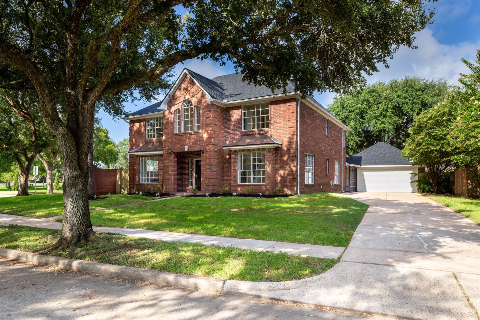 Beautiful two-story brick house with large windows. Theres a long driveway leading to a detached garage, creating a spacious and inviting exterior.