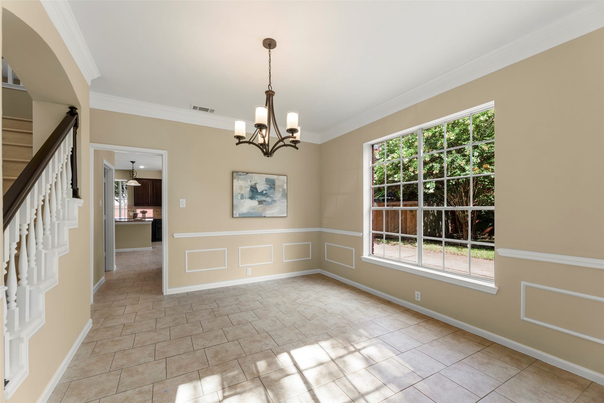 Elegant chandelier, features wainscoting, neutral walls, and a view of the staircase and kitchen entrance.