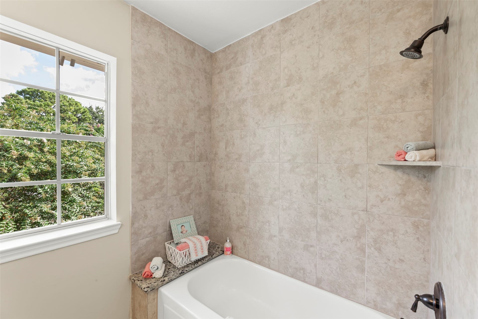 Window overlooking greenery. It includes a bathtub with a tiled shower area and elegant fixtures, offering a serene and inviting atmosphere.