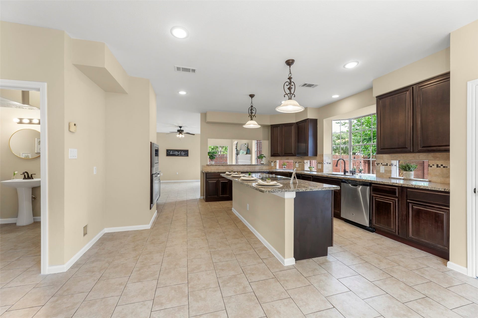 Centered island with pendant lighting and a large window providing ample natural light. Adjacent to a tiled hallway and nearby powder room.