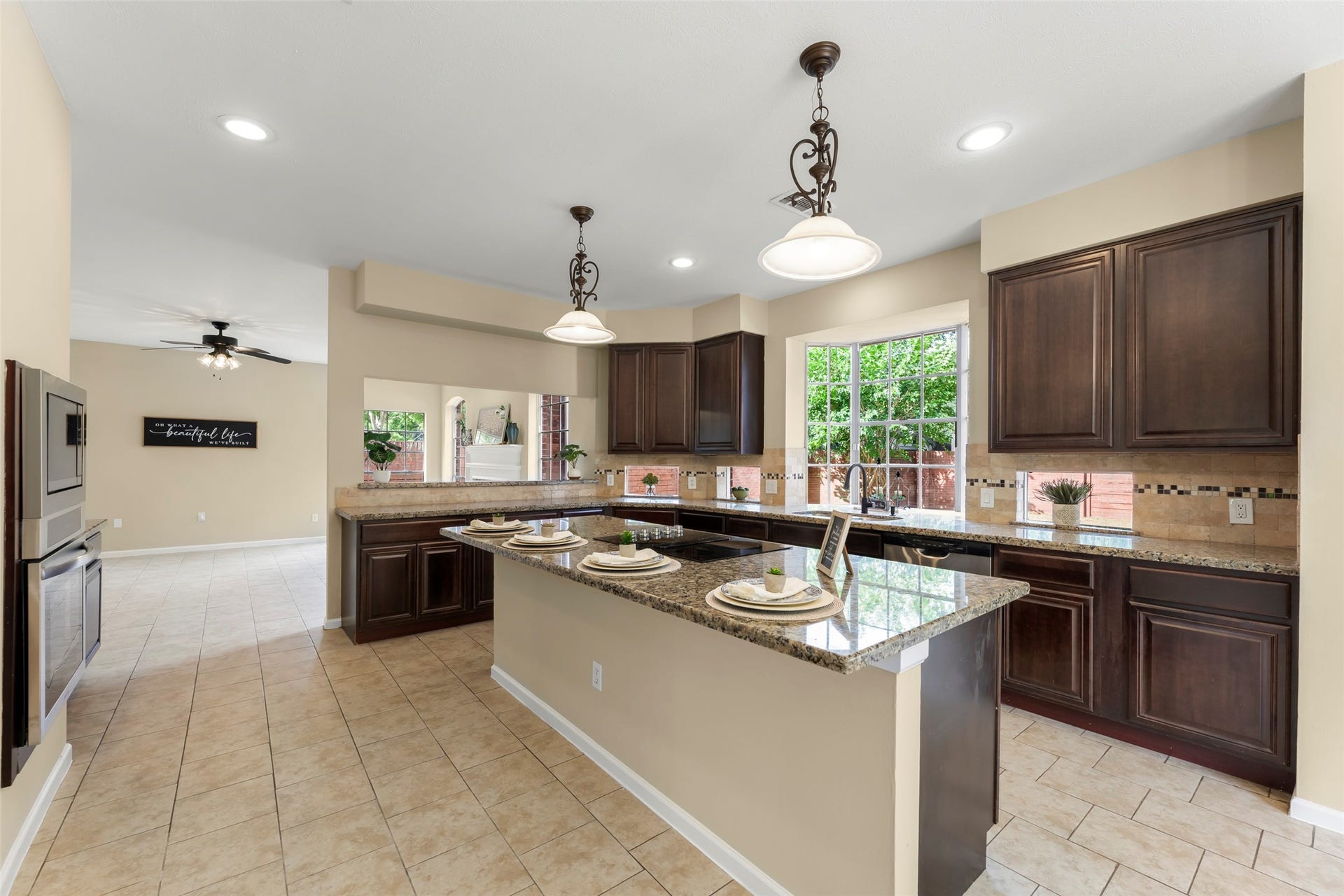 Ample natural light from large windows and includes a breakfast bar. The space flows into an open living area with a ceiling fan.