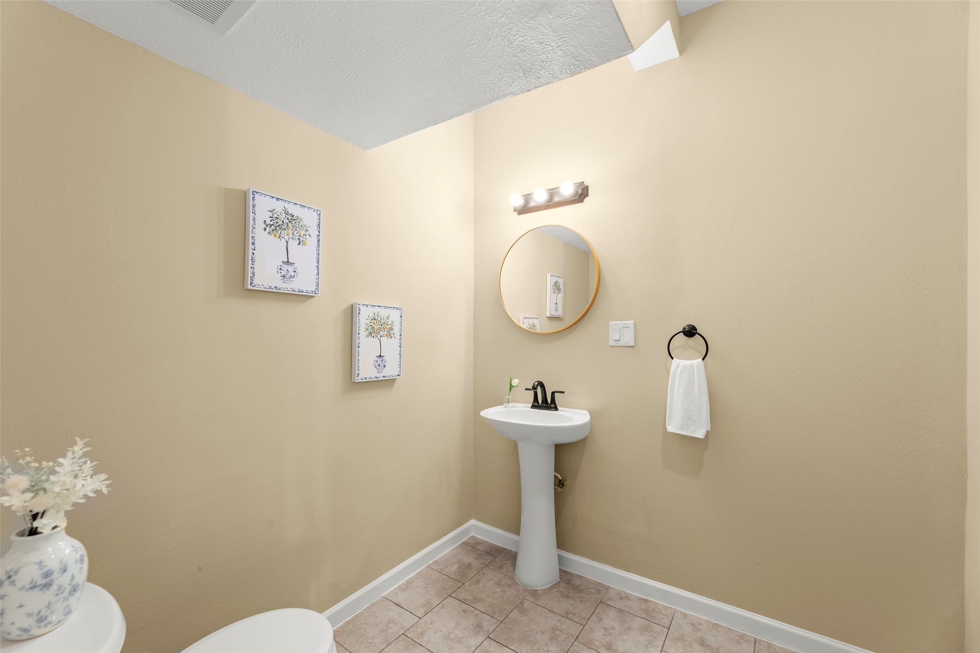 Well-lit powder room with a modern light fixture, and wall art adds a decorative touch. The tile flooring and simple decor create a clean, inviting atmosphere.