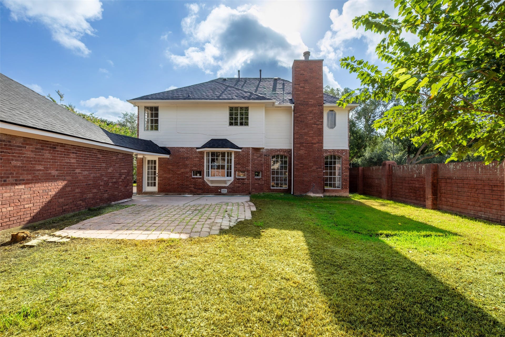 Paved patio. The exterior includes a prominent chimney, and the yard is surrounded by a brick wall, offering privacy.