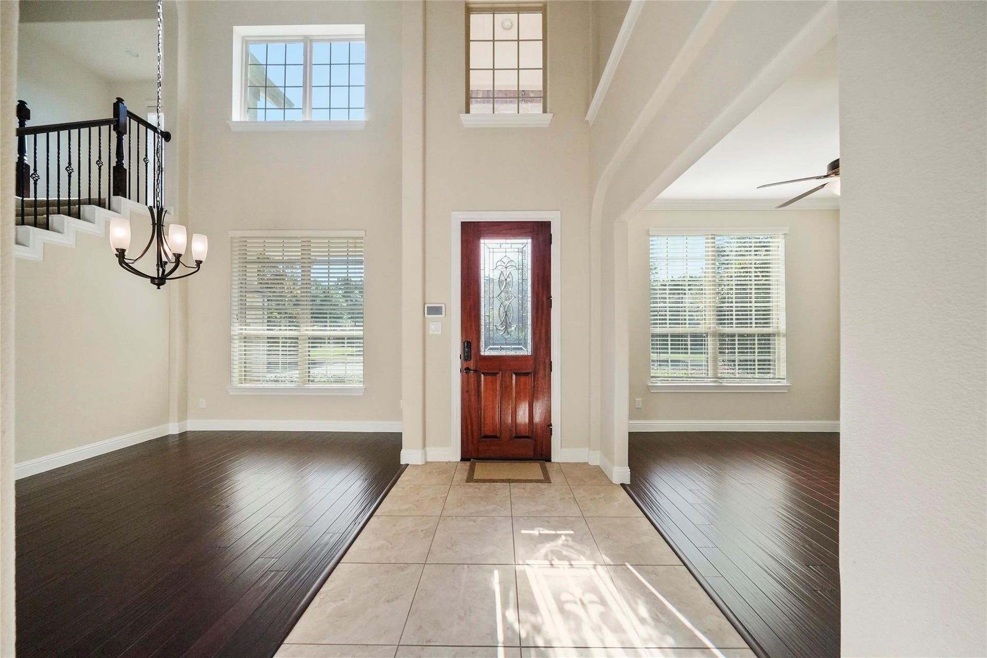 2026 Baker Estates Drive, Houston, TX 77094 Grand two-story foyer, showing the wood front door with decorative glass, hanging chandelier, staircase with iron railing, tile entry flanked by dark wood floors, and large windows with blinds.