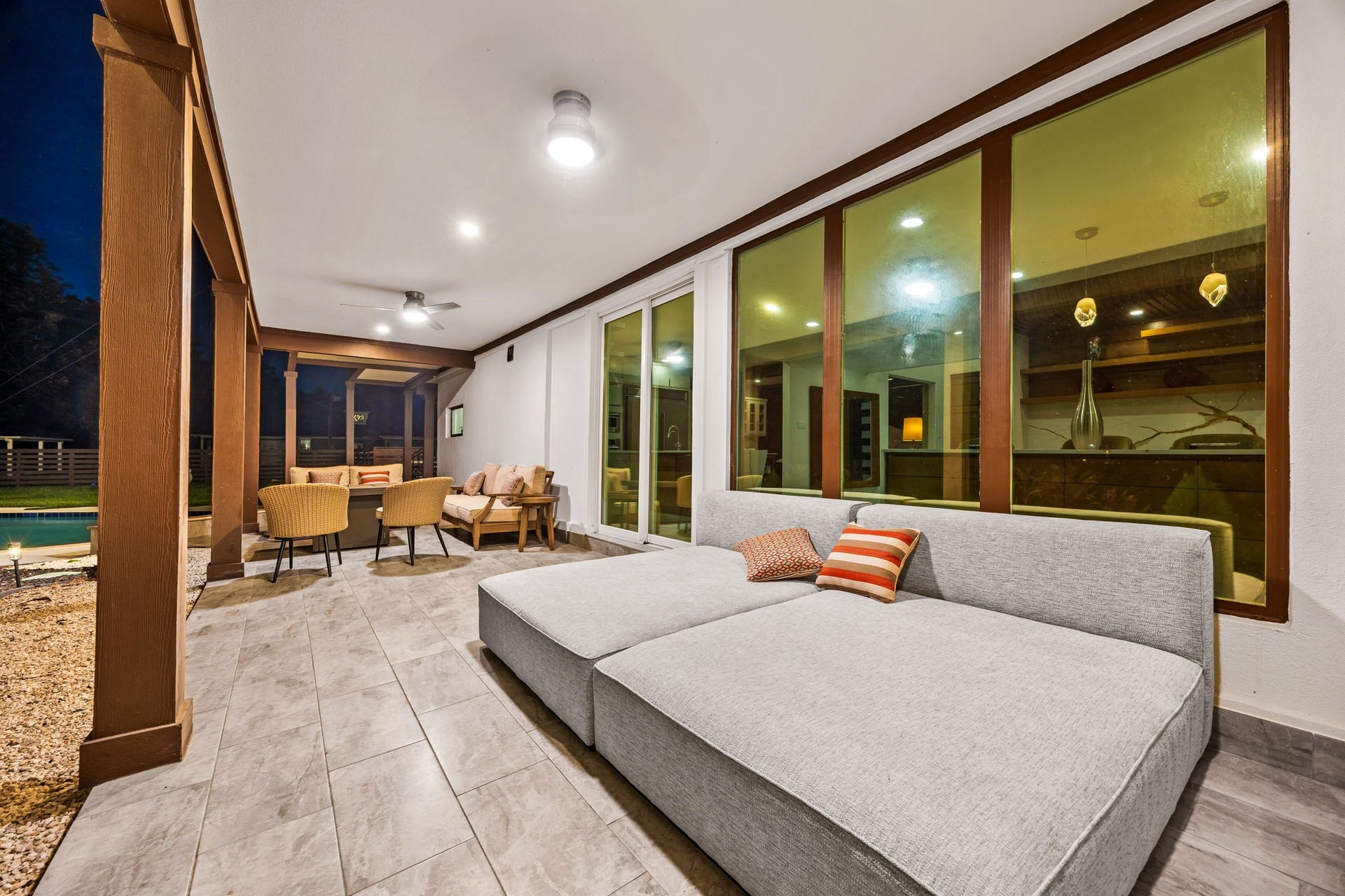 6830 Bois D Arc Lane, Fulshear, TX 77406 The covered patio extends the living space outdoors, with a plush daybed-style sectional, a cozy seating area, and glass doors connecting directly to the kitchen and living room.