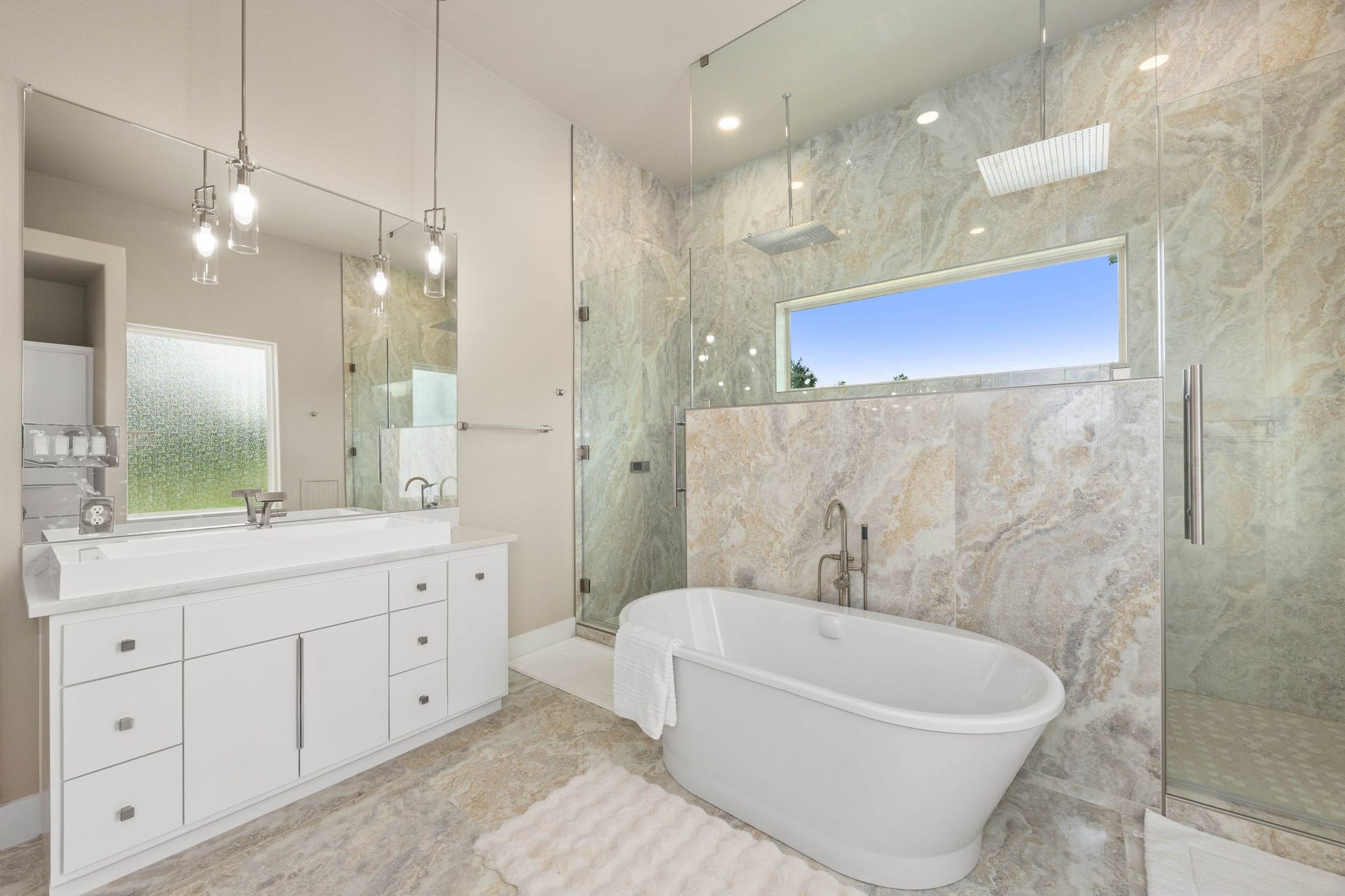 6830 Bois D Arc Lane, Fulshear, TX 77406 The primary bath features separate vanities, a freestanding soaking tub, and a glass-enclosed walk-in shower, all wrapped in floor-to-ceiling natural stone tile.