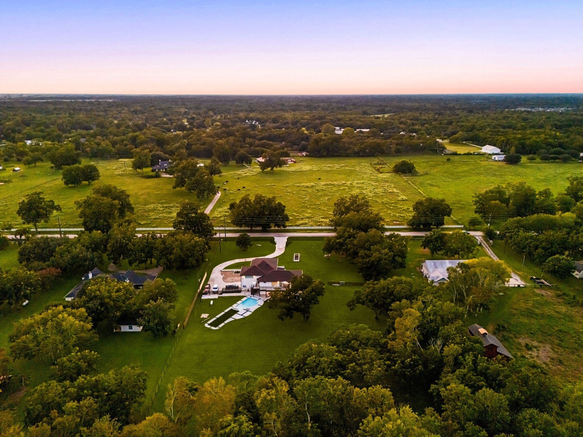 6830 Bois D Arc Lane, Fulshear, TX 77406 As the sun sets over the surrounding countryside, this aerial view captures the beauty, privacy, and expansive scale of the estate. Gas and plumbing connections are already in place for a future casita or guesthouse, offering added flexibility for multigenerational living or extended-stay guests.