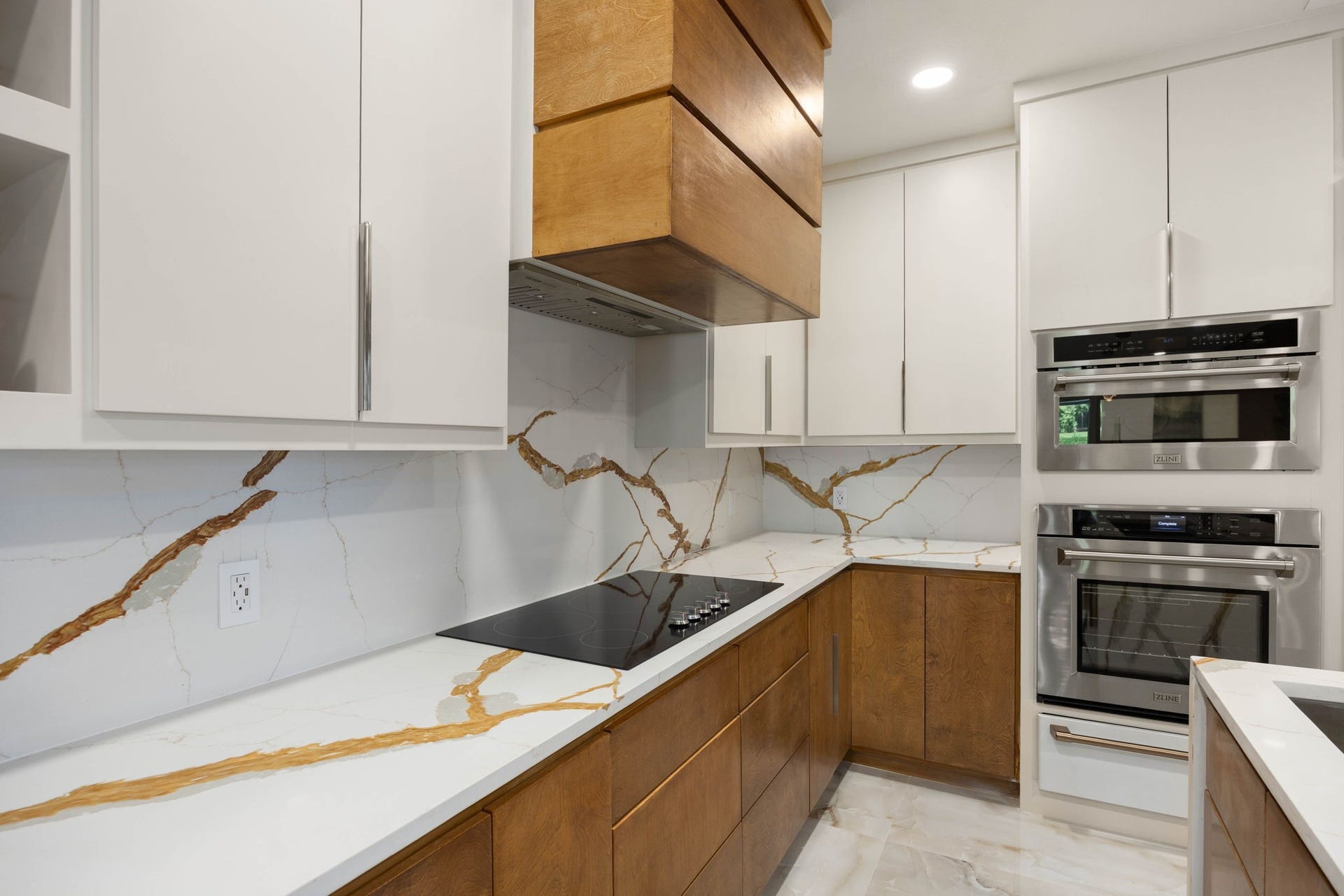 6830 Bois D Arc Lane, Fulshear, TX 77406 Bold veining sweeps across the countertops and backsplash, framing the cooktop in a wash of natural gold and white tones.