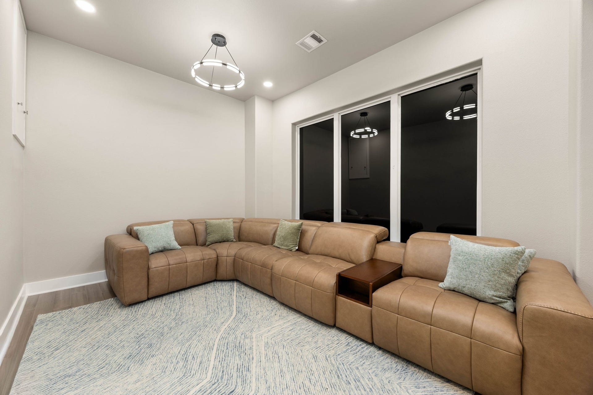6830 Bois D Arc Lane, Fulshear, TX 77406 This media room sits above the primary bedroom on the third floor, offering plush sectional seating beneath a modern pendant chandelier a relaxed spot for movie nights or casual gatherings.