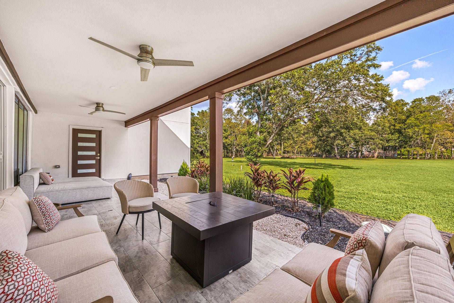 6830 Bois D Arc Lane, Fulshear, TX 77406 By day, the same patio offers additional lounge seating around a fire pit table, with ceiling fans and open views of the tree-lined backyard.