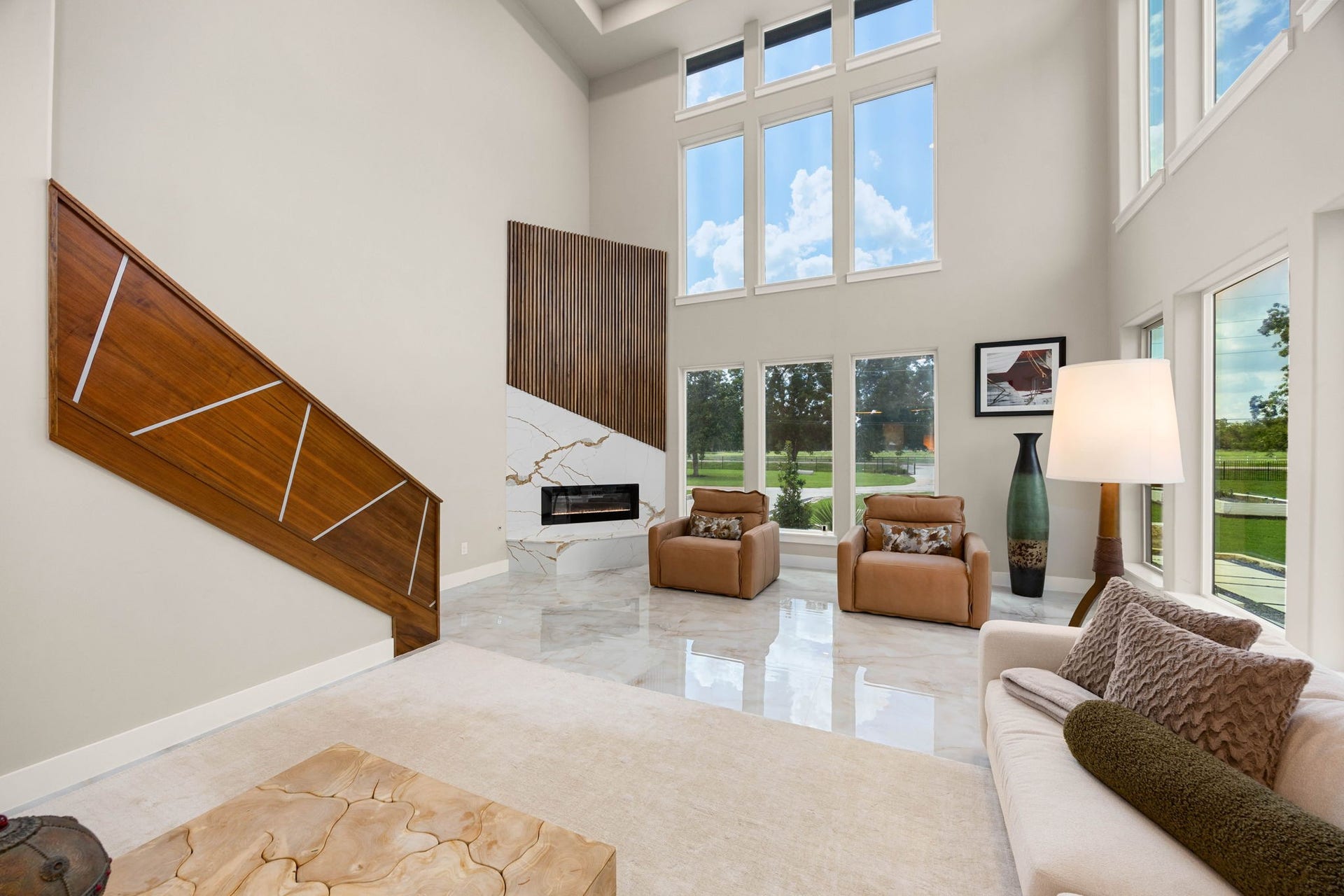 6830 Bois D Arc Lane, Fulshear, TX 77406 A dramatic wood-slatted fireplace wall rises alongside soaring two-story windows, framing the living area's serene garden views.