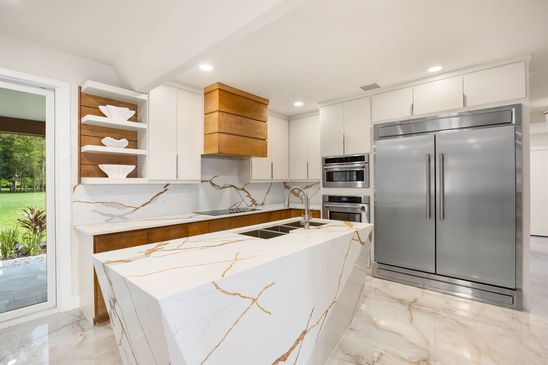 6830 Bois D Arc Lane, Fulshear, TX 77406 Professional-grade stainless appliances, a wood-paneled range hood, and floor-to-ceiling marble backsplash define this kitchen's polished, functional design.