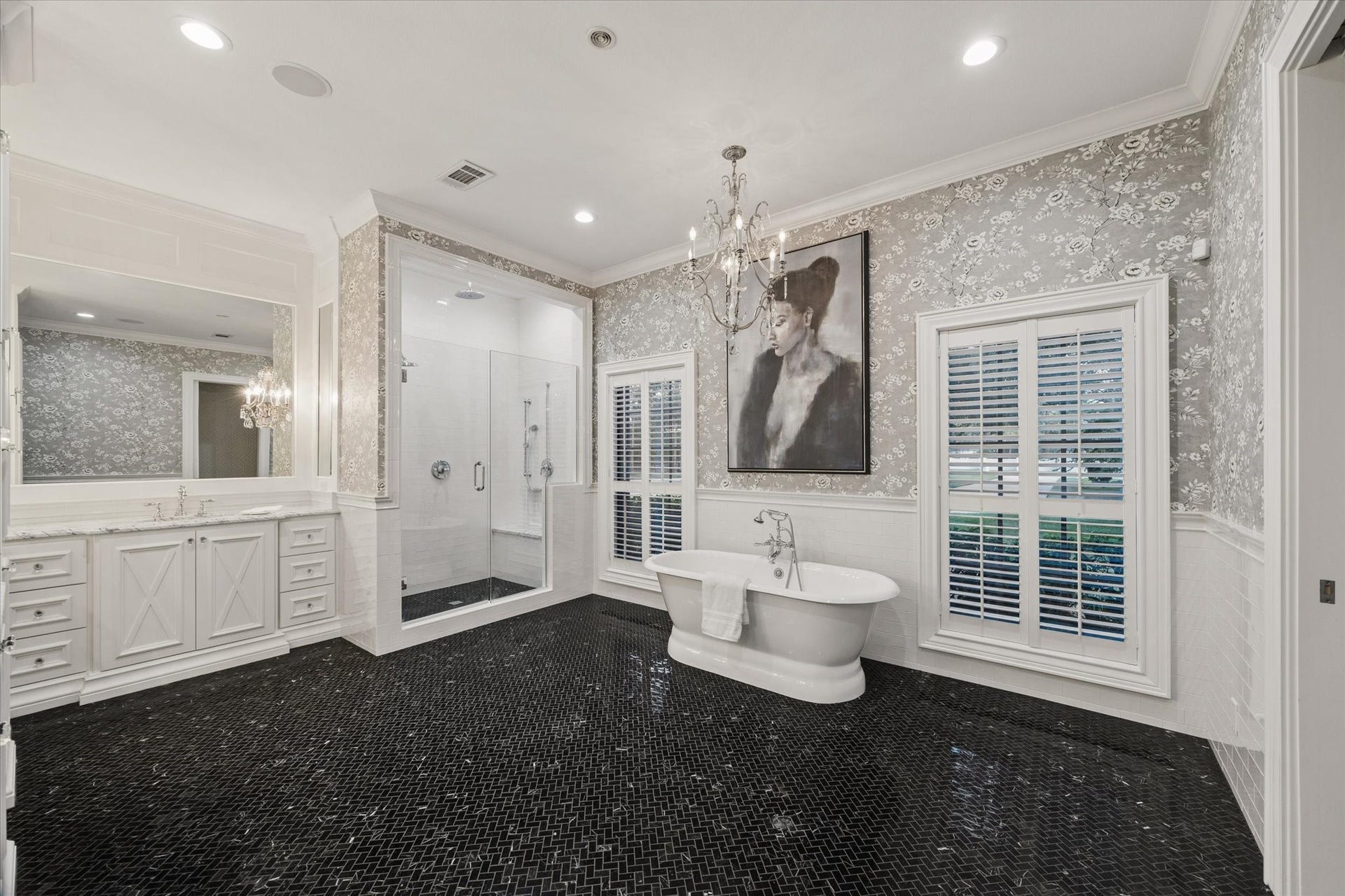 Luxurious bathroom with elegant black tile flooring, a freestanding tub, glass-enclosed shower, and stylish vanity, all accented by chic wallpaper and a chandelier.