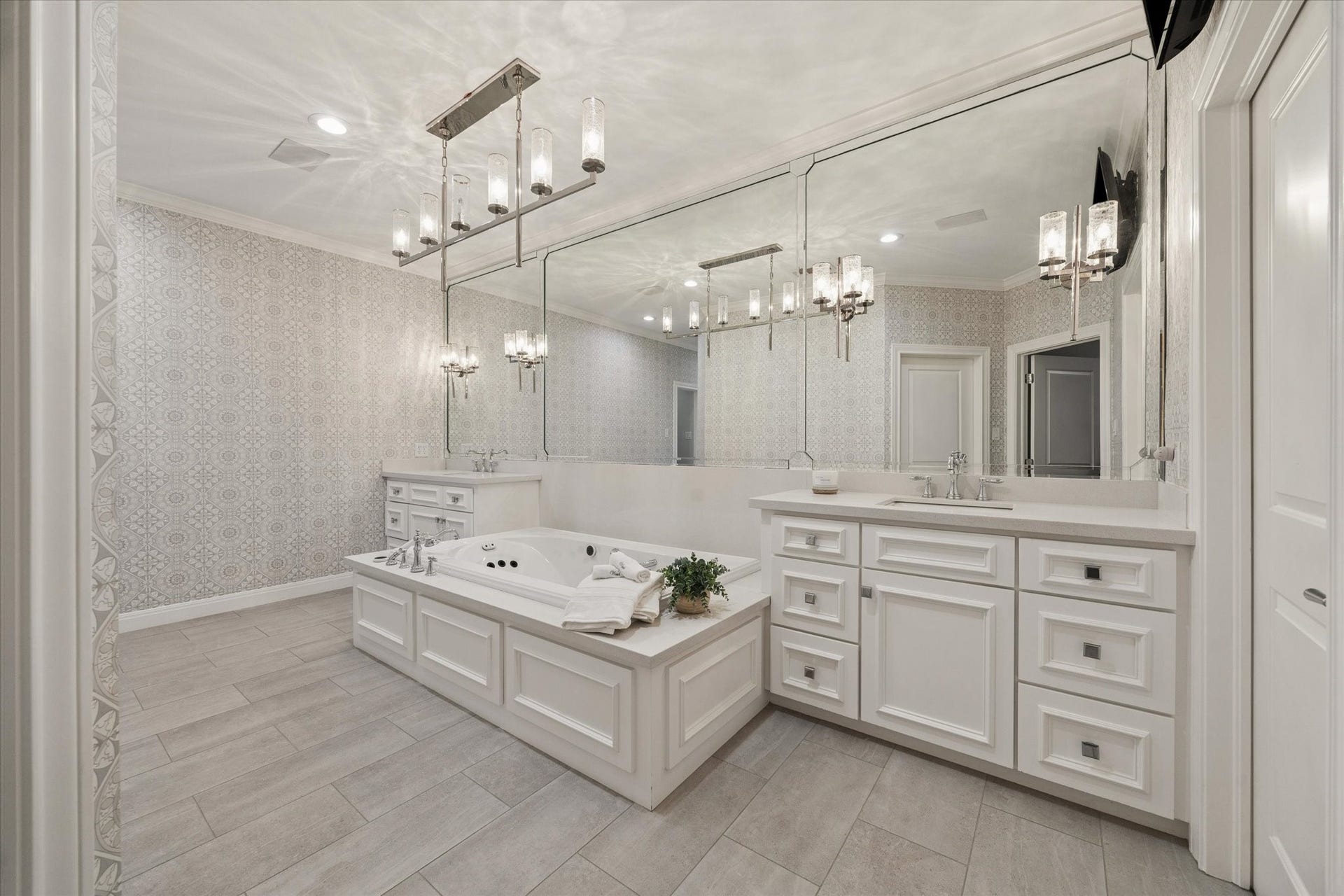 Second floor primary bath featuring a jetted soaking tub, elegant custom wallpaper, and dual walk-in closets.