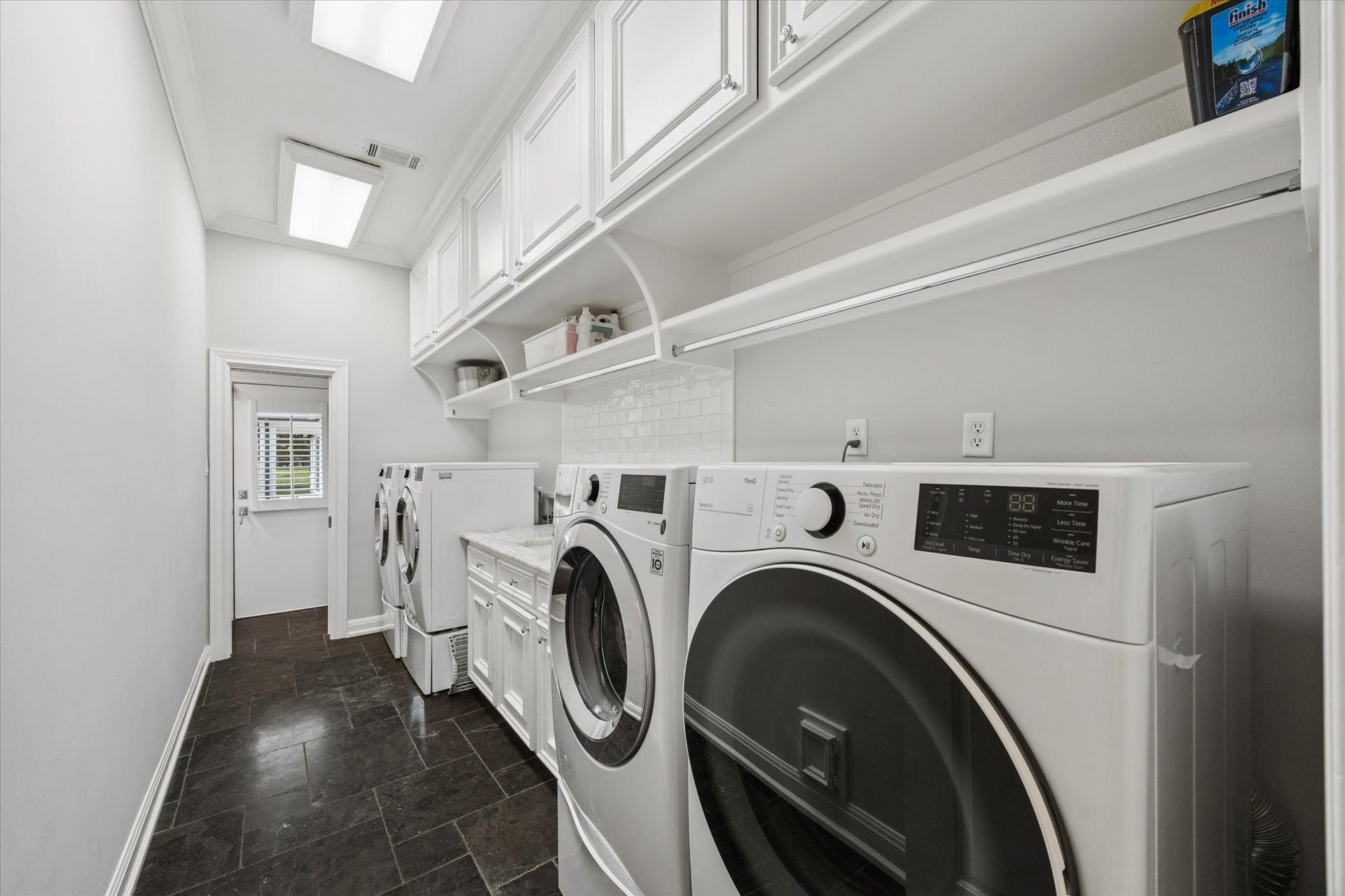 Laundry room with ample storage and limestone flooring. There hook ups for two sets of laundry, a sink and a powder bath that leads out to the pool and patio.
